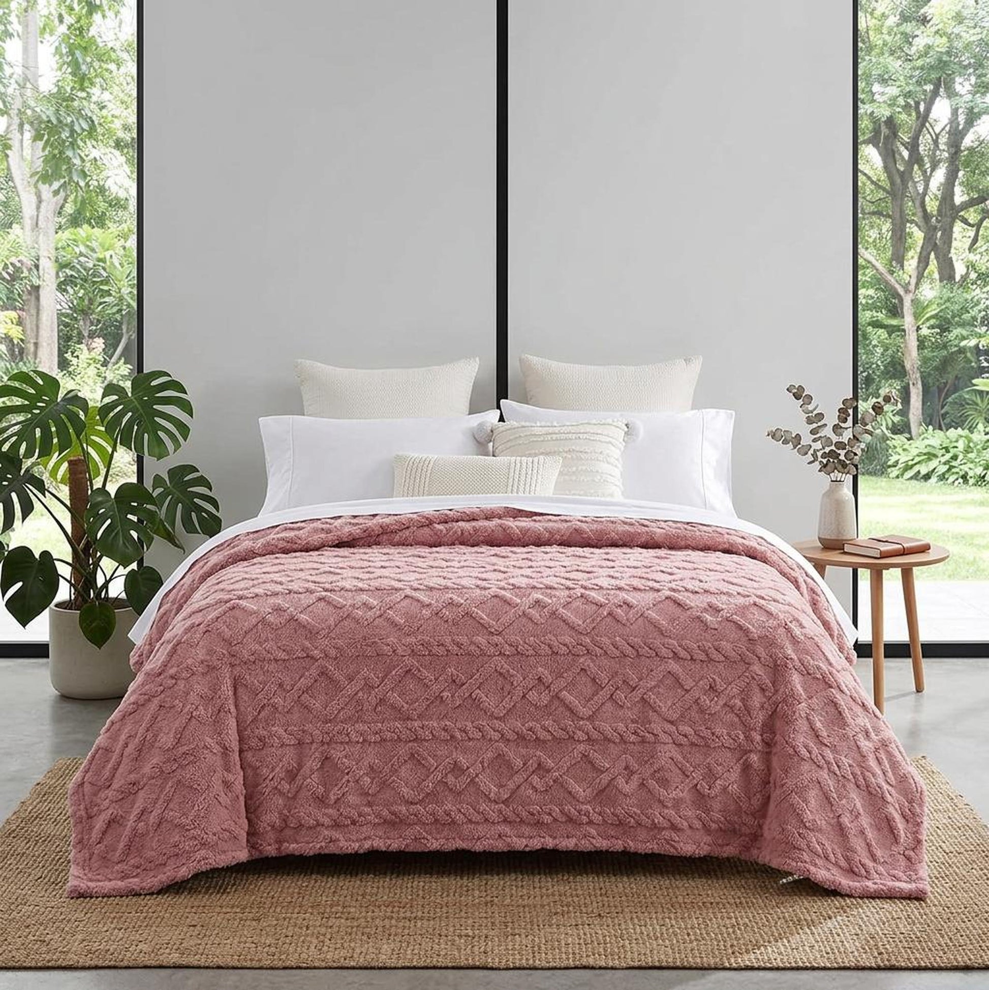 Pink ruched faux fur throw blanket on a bed with white pillows in a bright room.