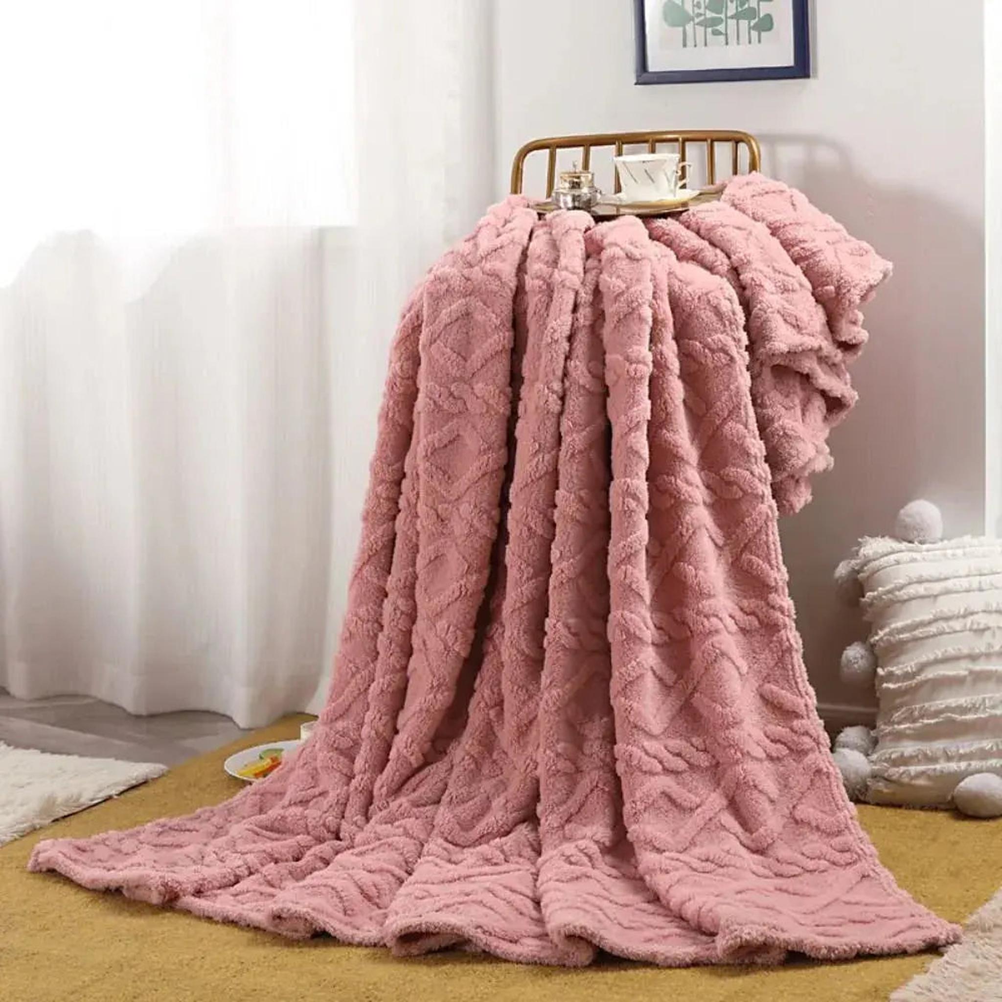 Pink ruched faux fur throw blanket draped over a chair, showcasing its soft texture and double-sided design.