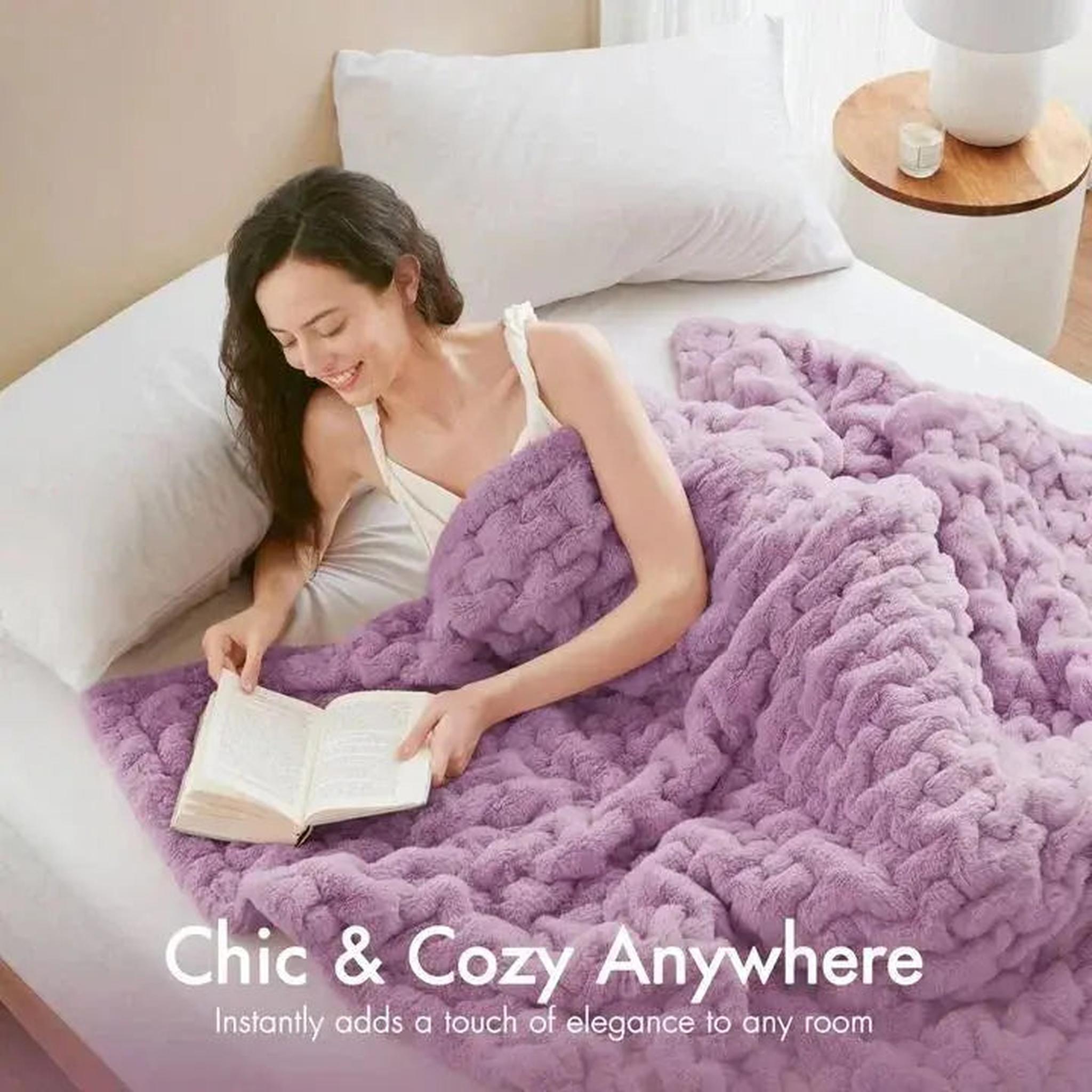 Woman reading in bed, covered by a soft, ruched lavender faux fur throw blanket.