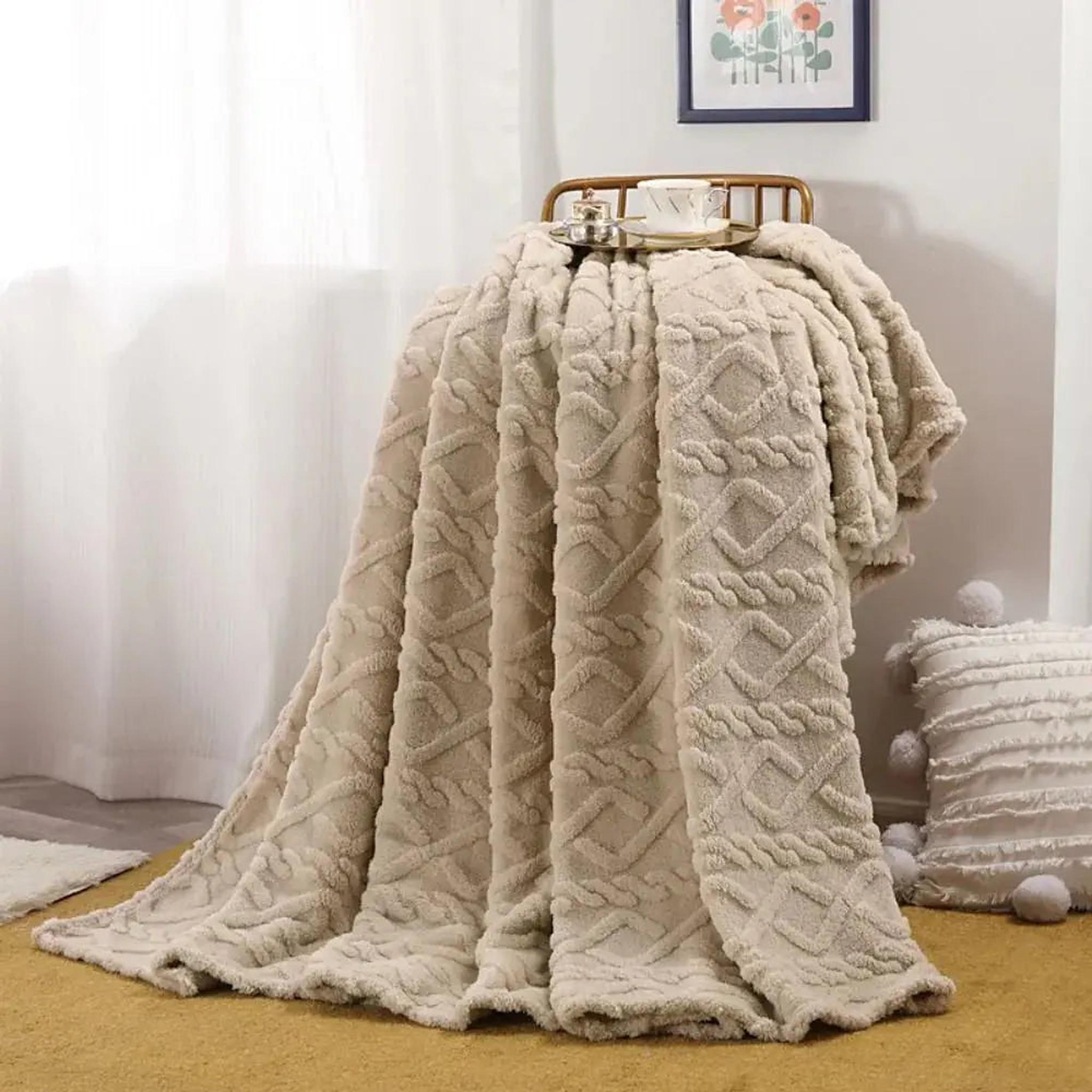 Beige ruched faux fur throw blanket draped over a chair, with a cup on top.