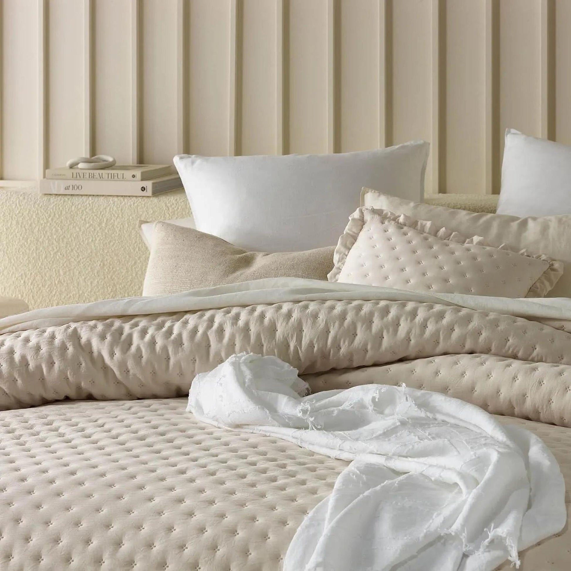 Lightweight beige ruffle mattress cover quilt with scalloped edge and textured pillows on a bed.
