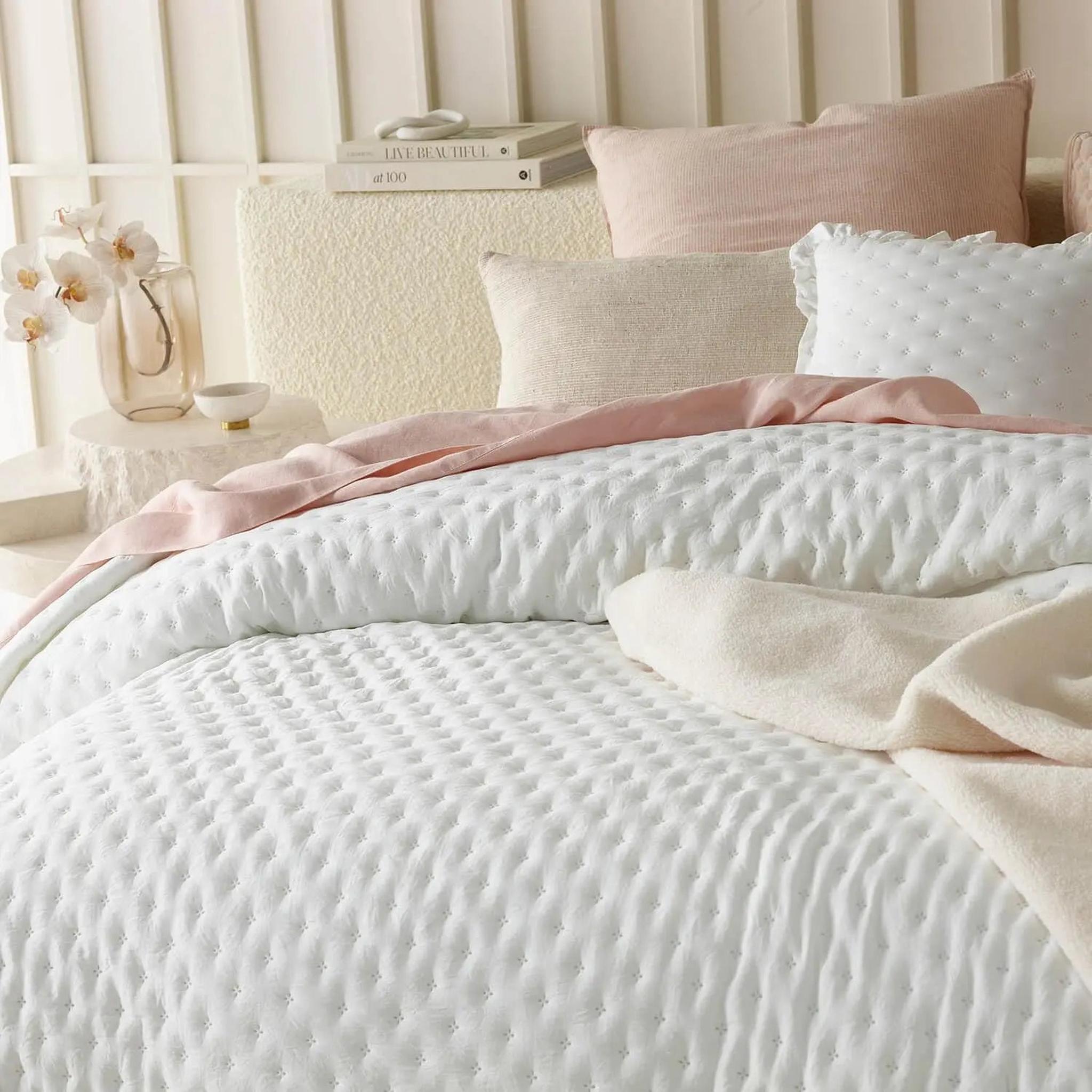 White ruffle mattress cover quilt with scalloped edge, layered with pink and cream bedding.