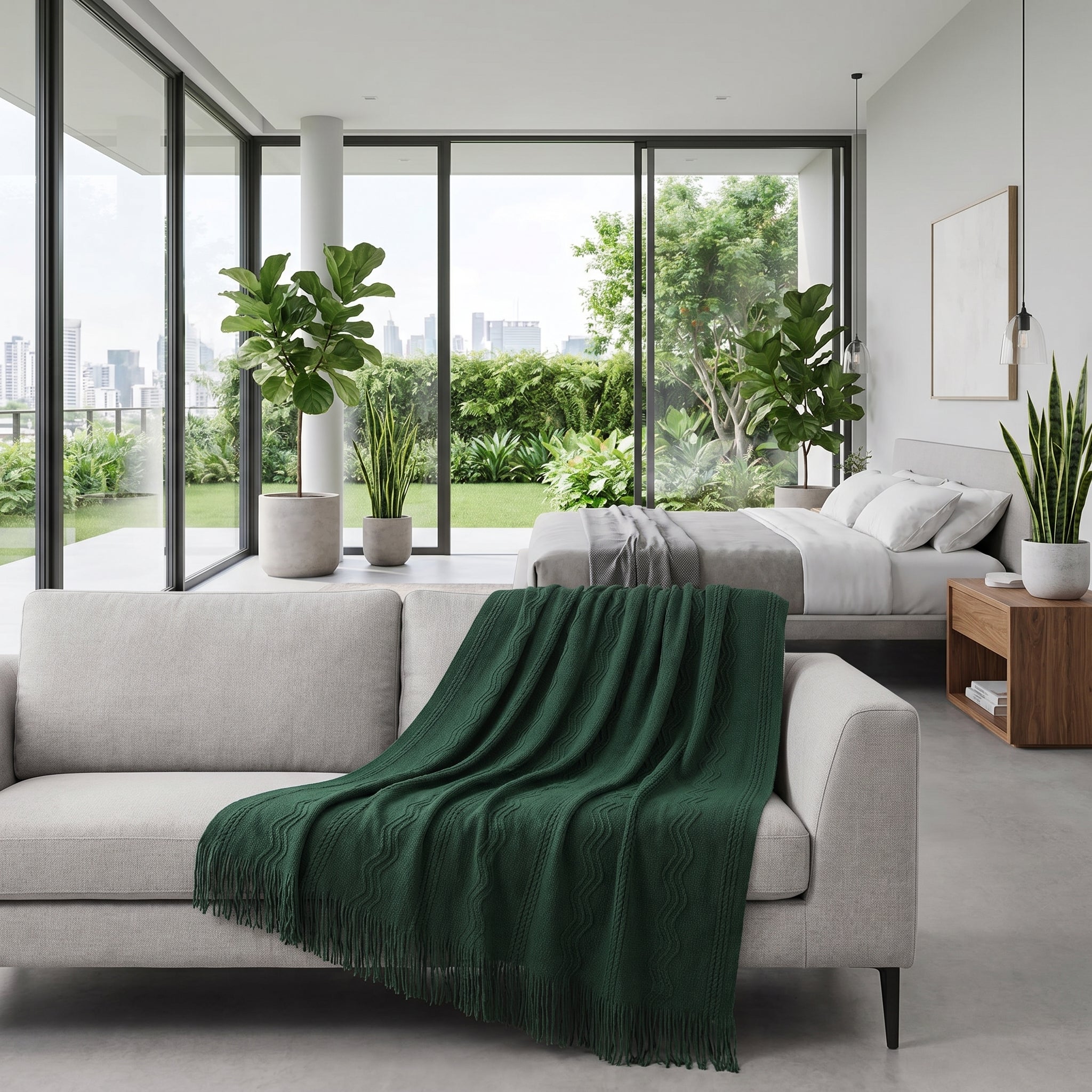 Sage green knitted throw blanket with fringe draped over a light gray sofa in a modern room.