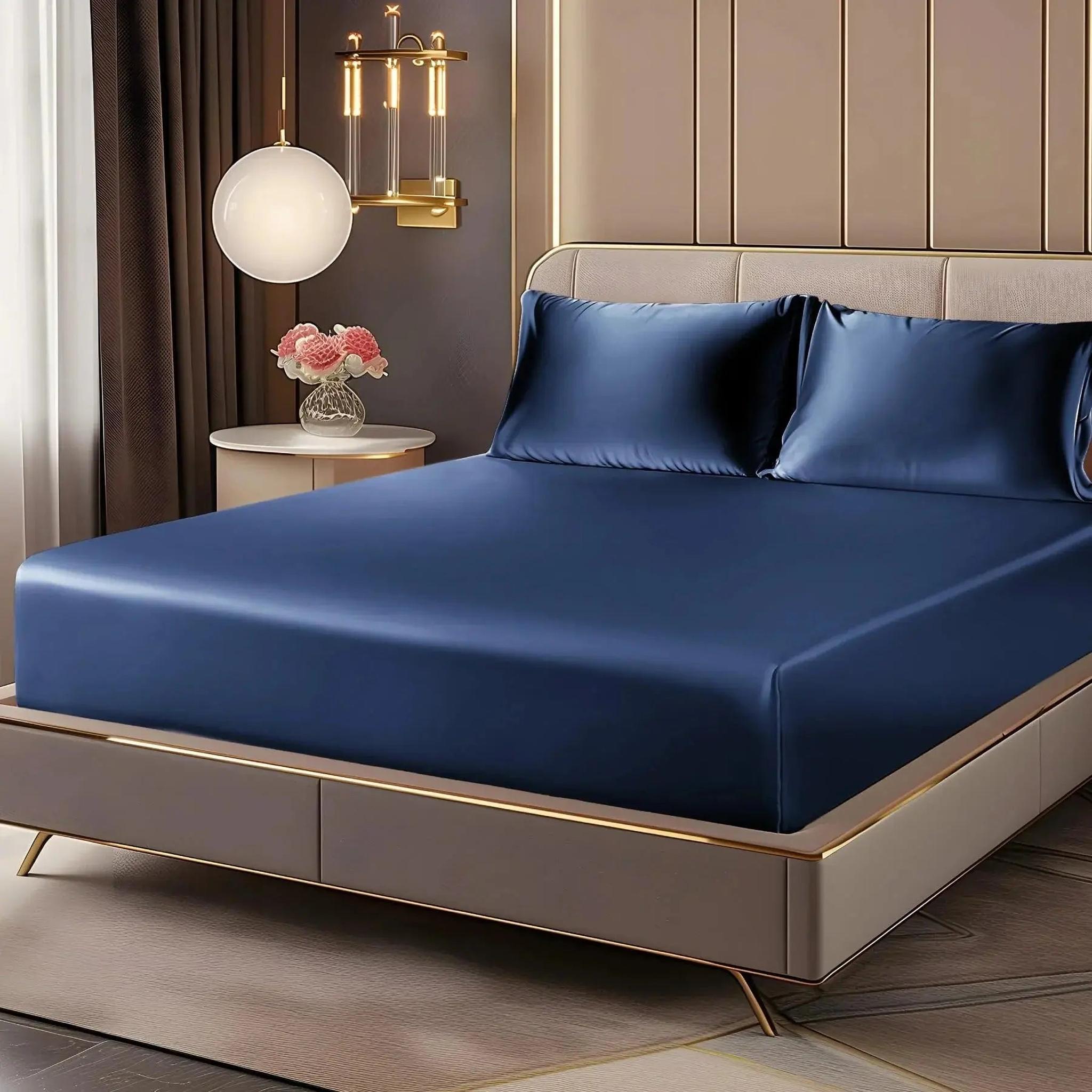 Elegant navy blue satin fitted sheet set with two pillowcases on a bed in a modern bedroom.