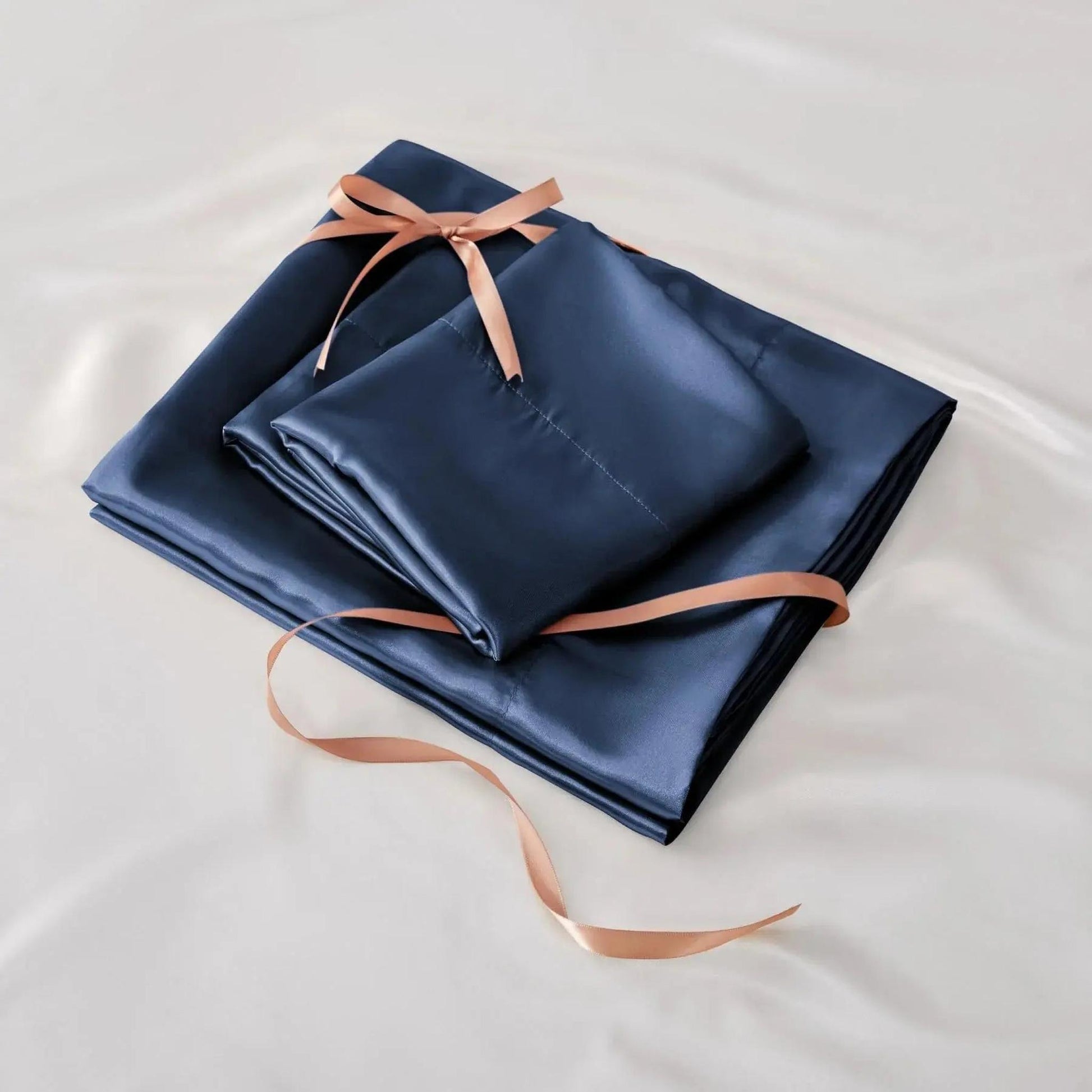 Navy blue satin fitted sheet set with matching pillowcases, tied with a copper ribbon on white satin.