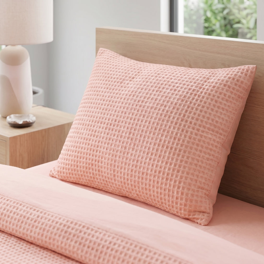 Soft pink waffle-weave cotton duvet cover set on a bed in a bright, modern bedroom with plants.