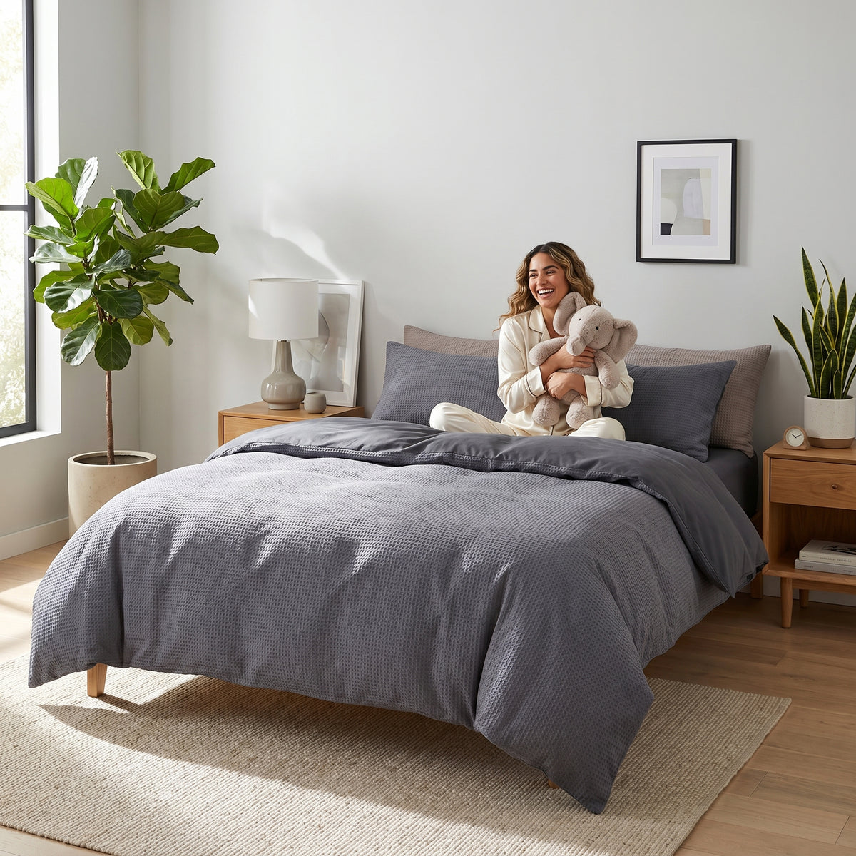 Woman sitting on a bed with a charcoal grey waffle-textured cotton duvet cover set in a bright, modern bedroom.