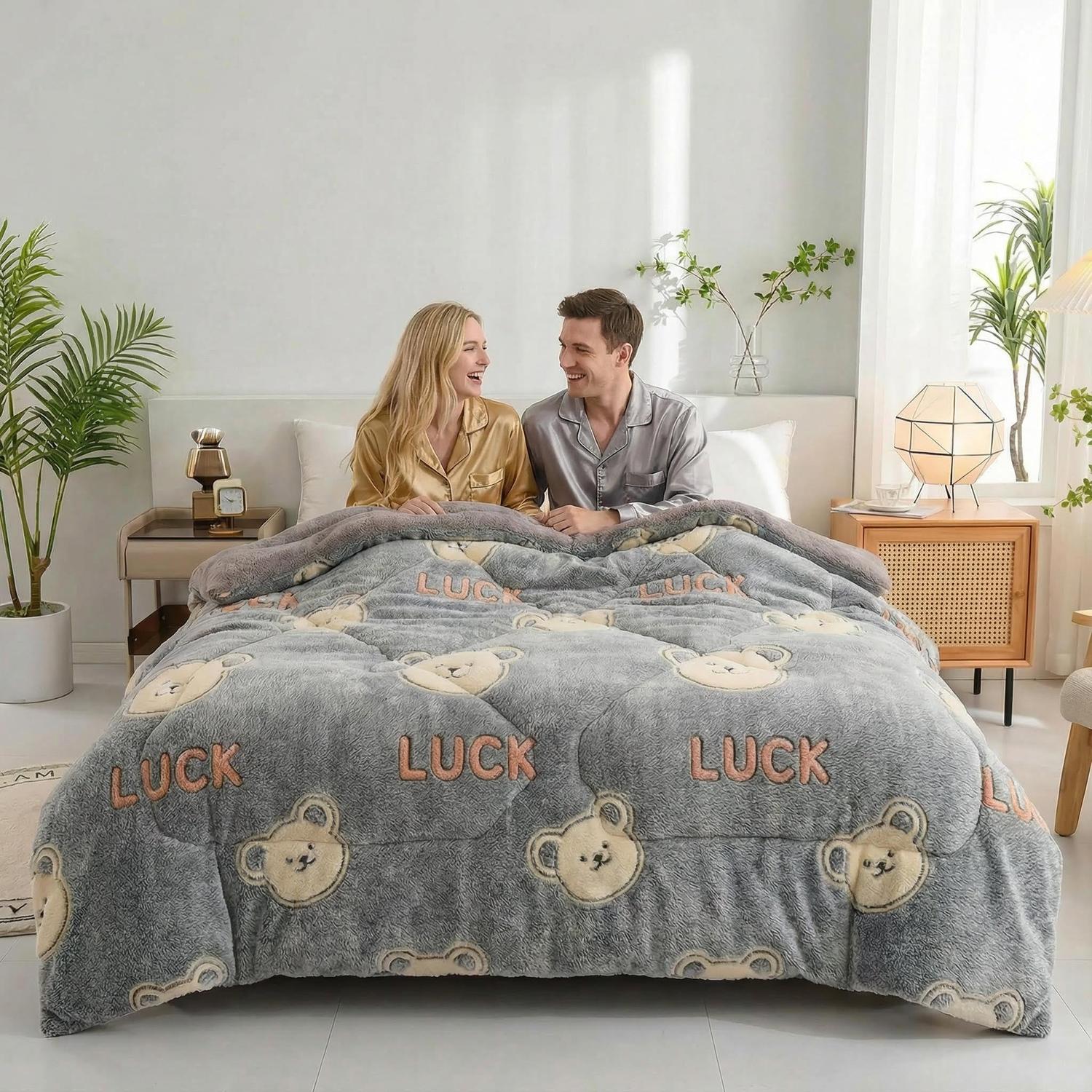 Couple on a bed with a gray velvet quilt featuring teddy bears and "LUCK" text.