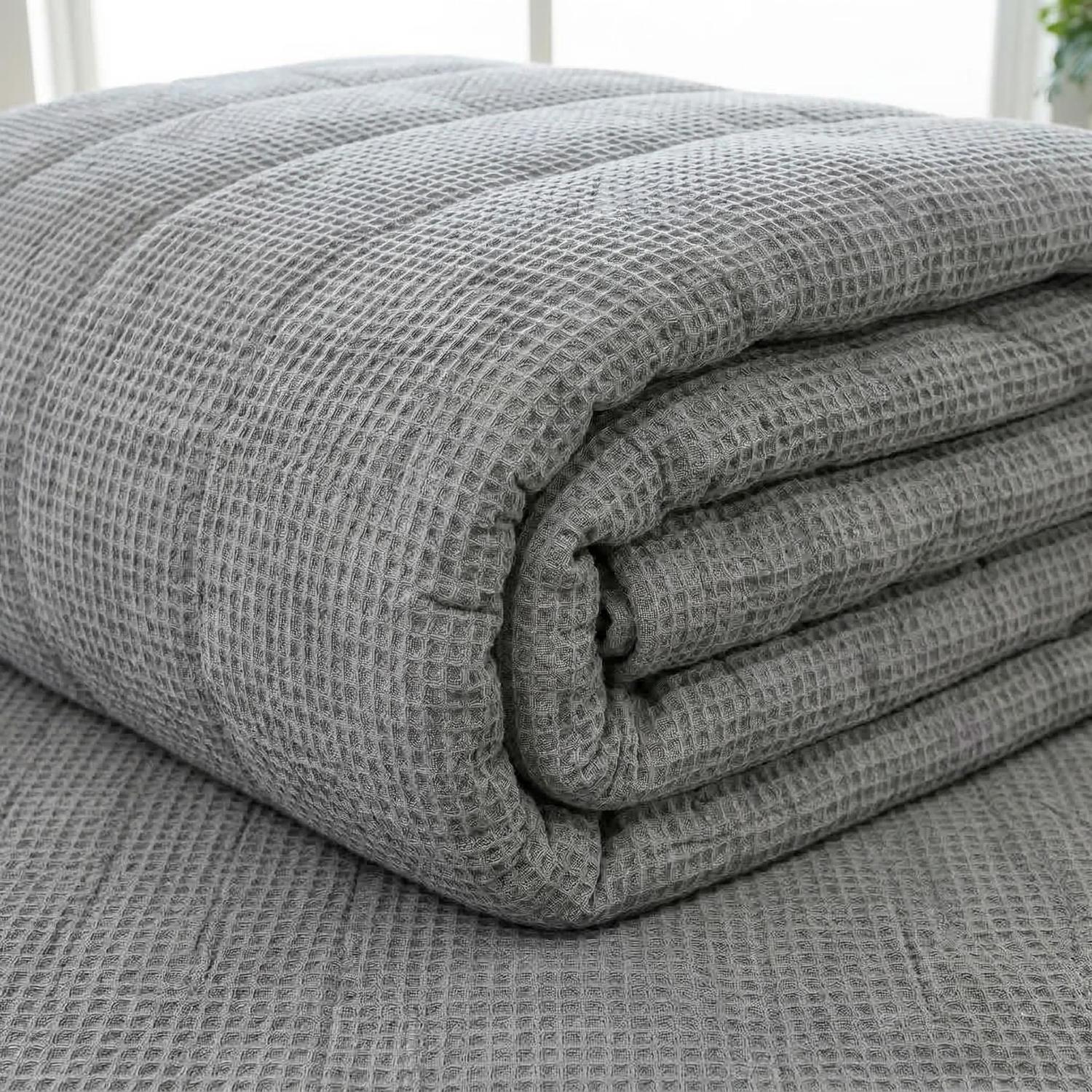 Soft gray muslin cotton bedspread with a geometric knitted waffle texture, folded on a matching surface.