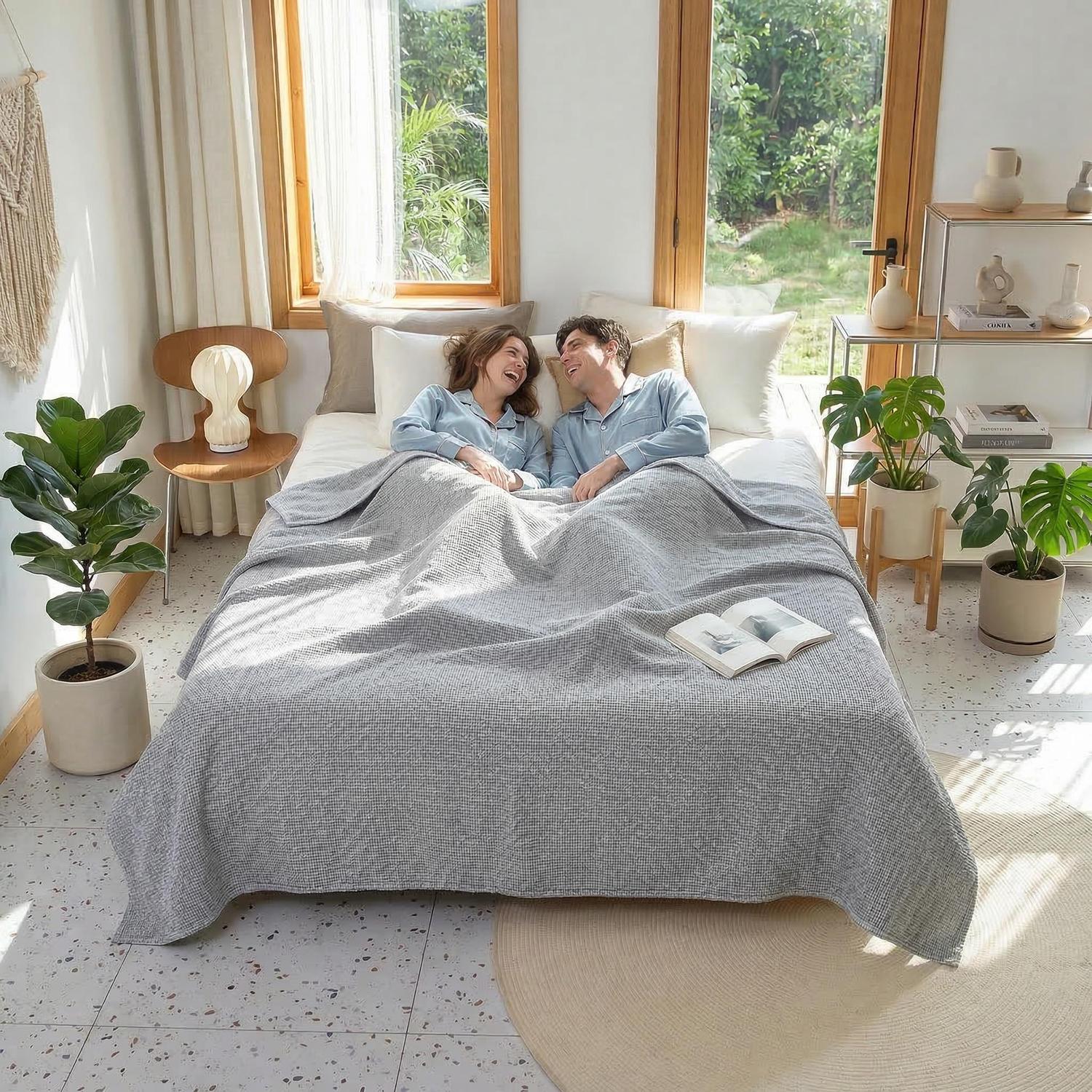 Couple laughing in bed under a soft gray muslin cotton bedspread with a geometric knit texture, in a bright bedroom.