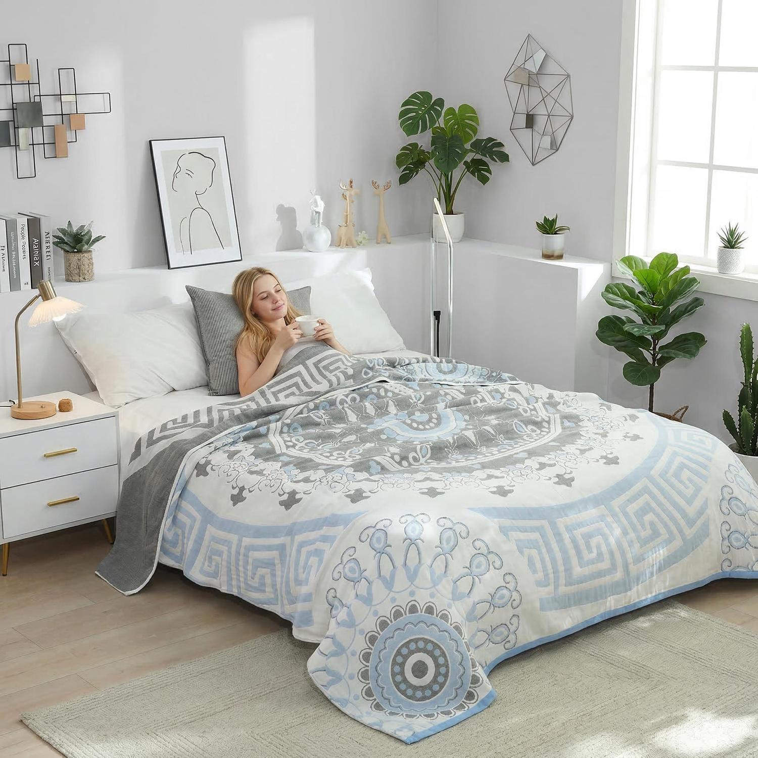 Woman relaxing in bed under a soft cotton summer quilt blanket with a blue and gray geometric mandala design.