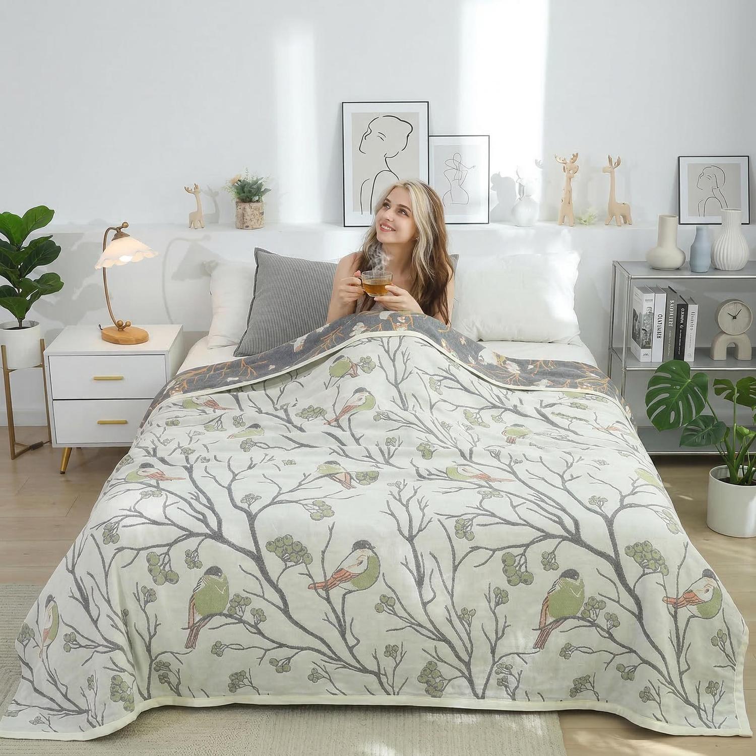 Soft cotton bedspread with green bird and tree branch pattern, covering a woman in a bright bedroom.