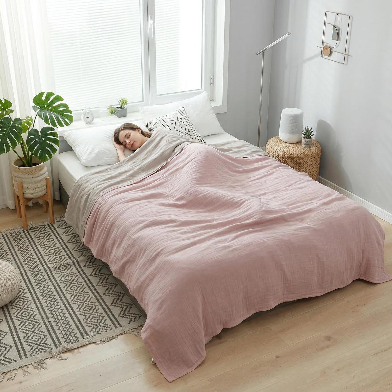 Woman sleeping under a soft pink and beige muslin cotton bedspread on a light wood floor.