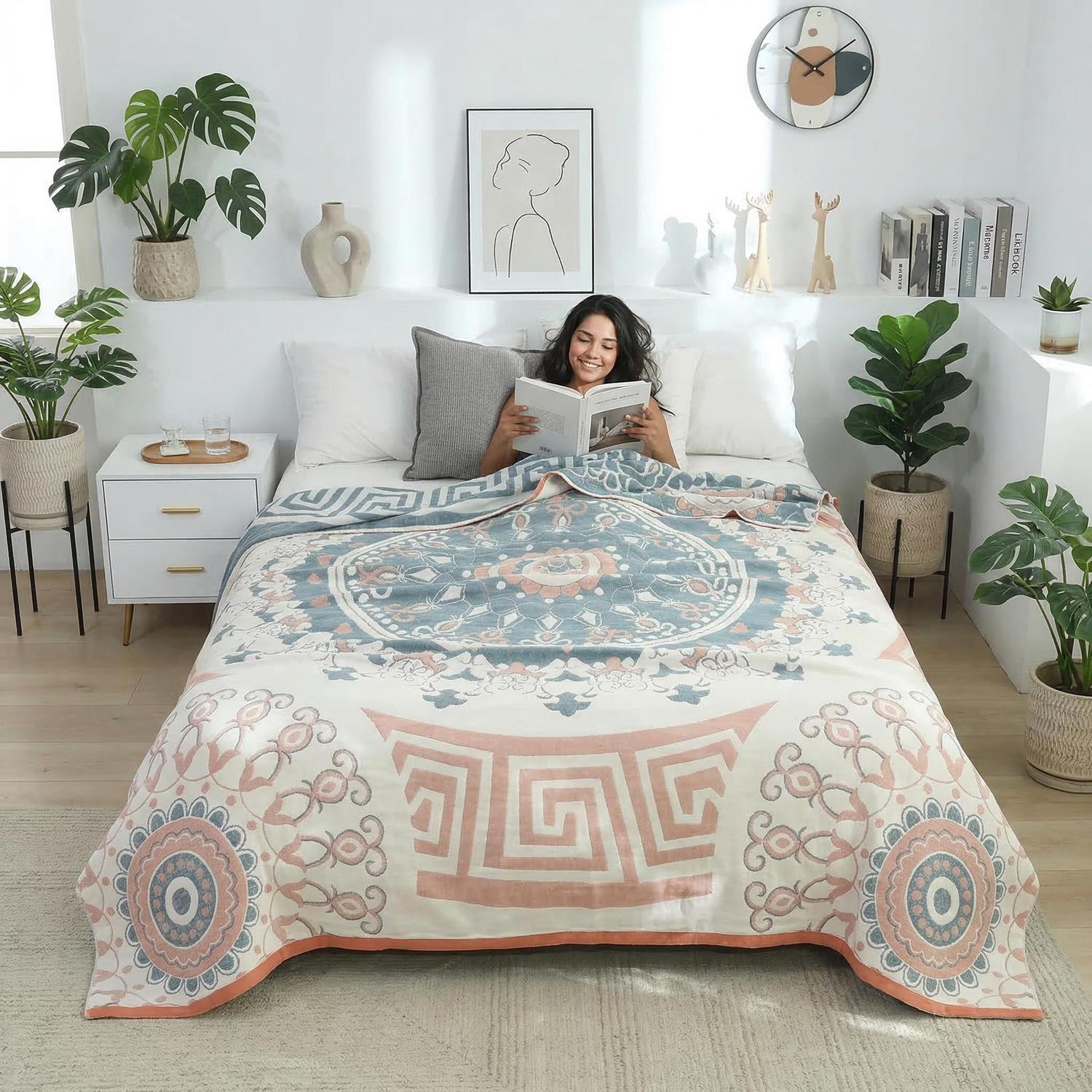 Woman reading in bed under a soft cotton summer quilt blanket with blue, peach, and white geometric mandala patterns.