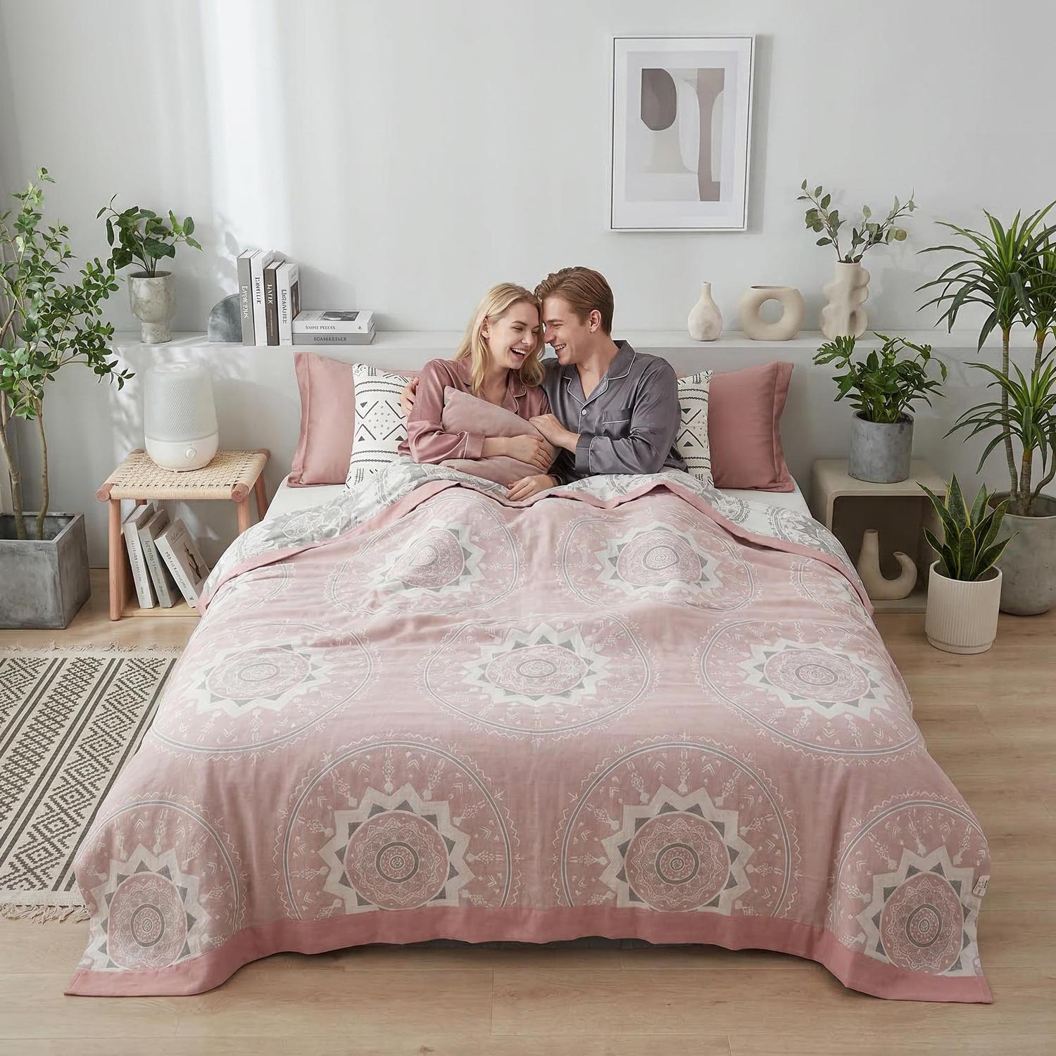 Couple smiling in bed under a pink cotton bedspread with a white geometric mandala pattern.