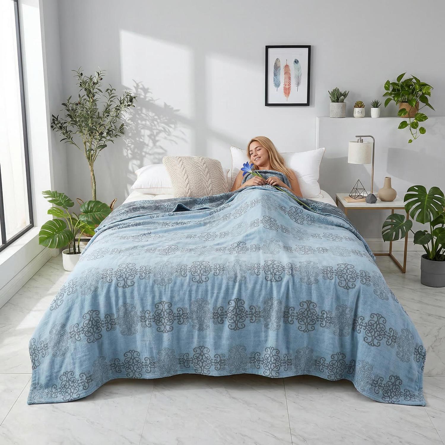 Woman relaxing in bed under a blue muslin cotton bedspread with a gray geometric knitted pattern.