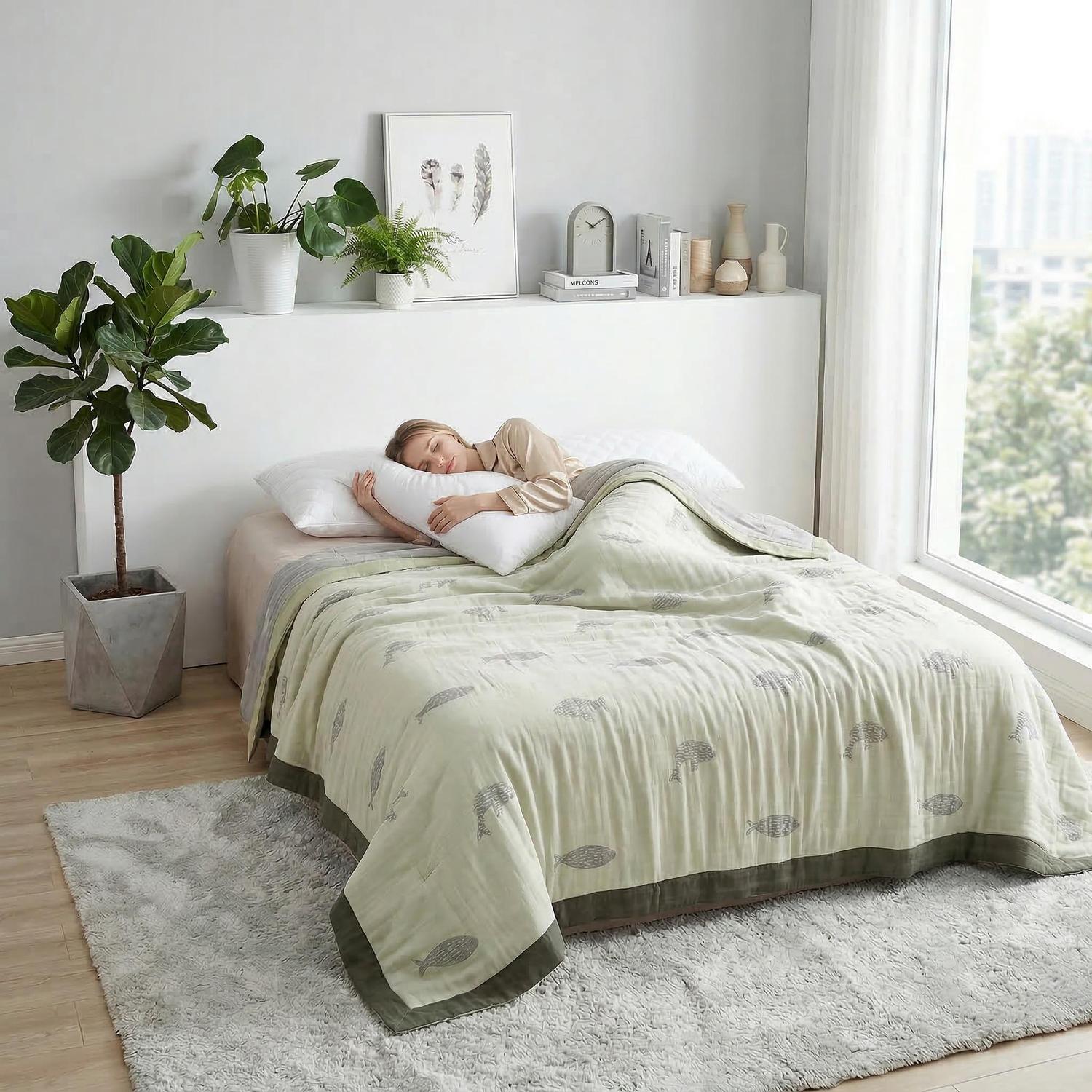 Woman sleeping under a soft cotton bedspread with a light green fish pattern and dark green border.