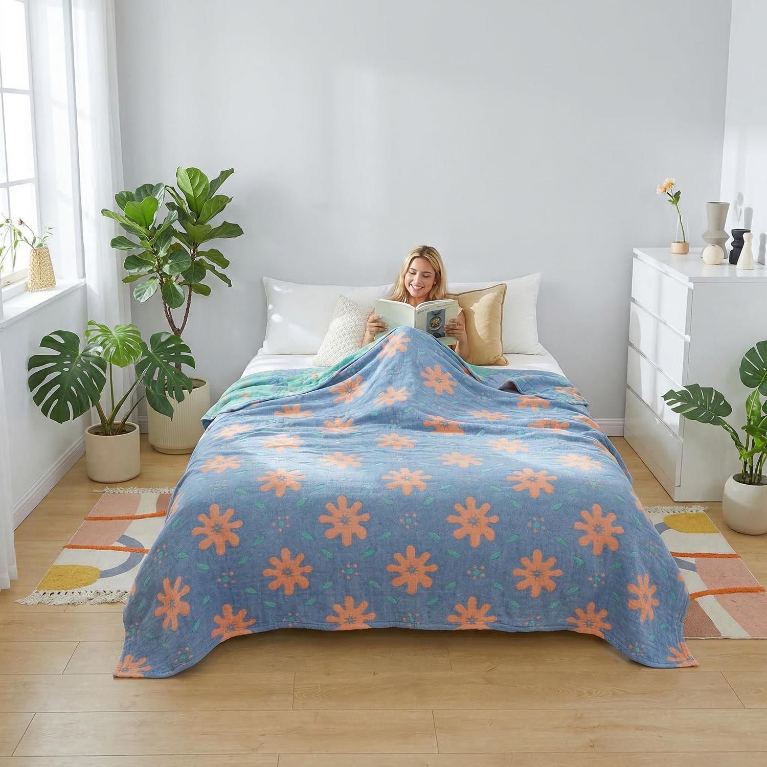 Woman smiling, reading in bed under a blue muslin cotton bedspread with orange floral print.