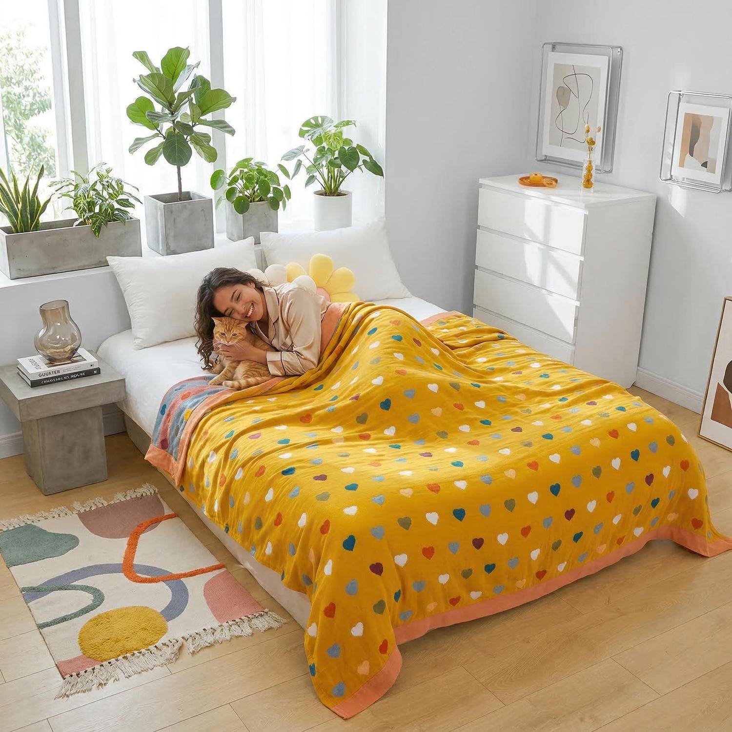 Smiling woman and cat on a bed covered with a yellow muslin cotton bedspread featuring colorful heart patterns.