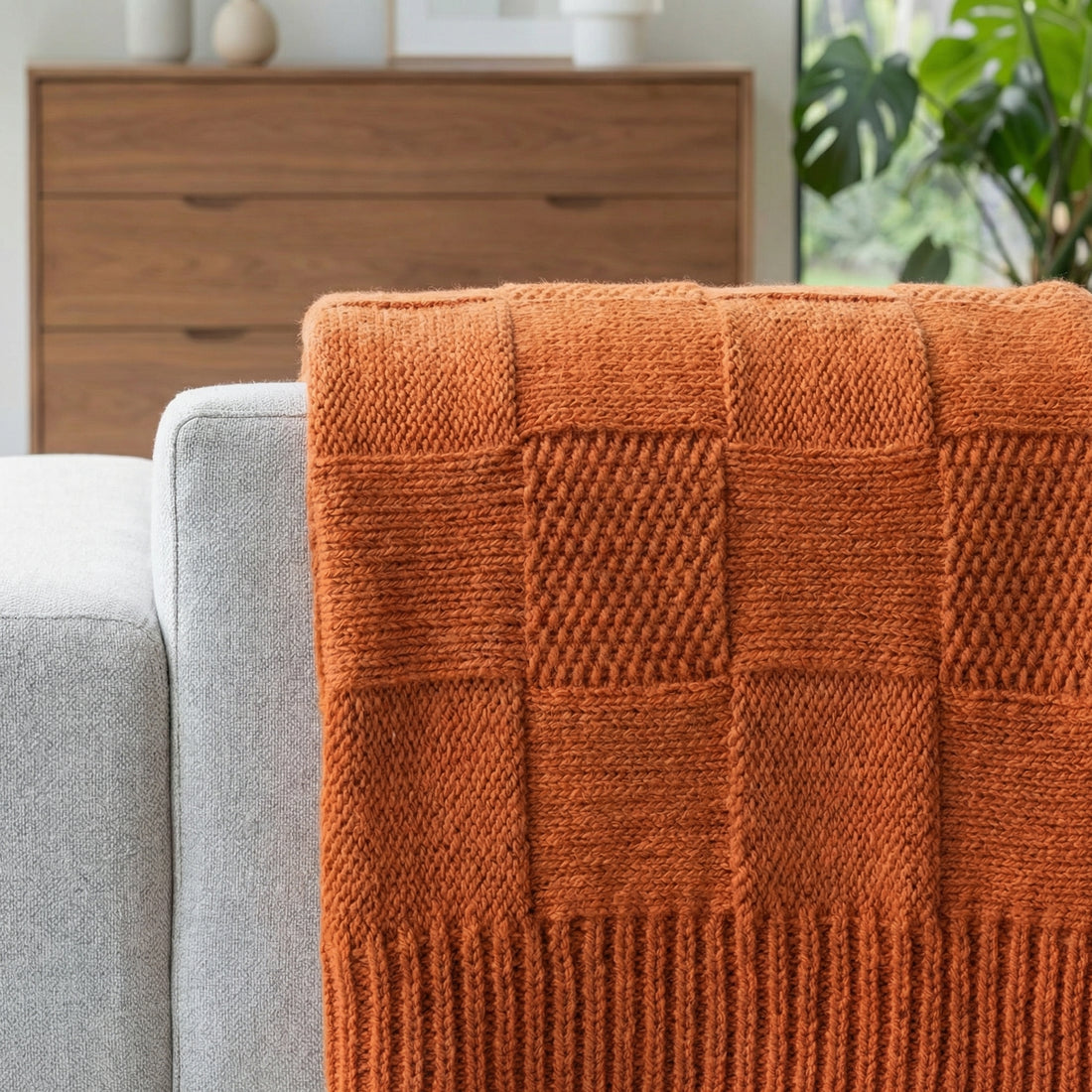 Smiling woman on a sofa, wrapped in a cozy, orange knitted cotton blanket with a textured pattern.