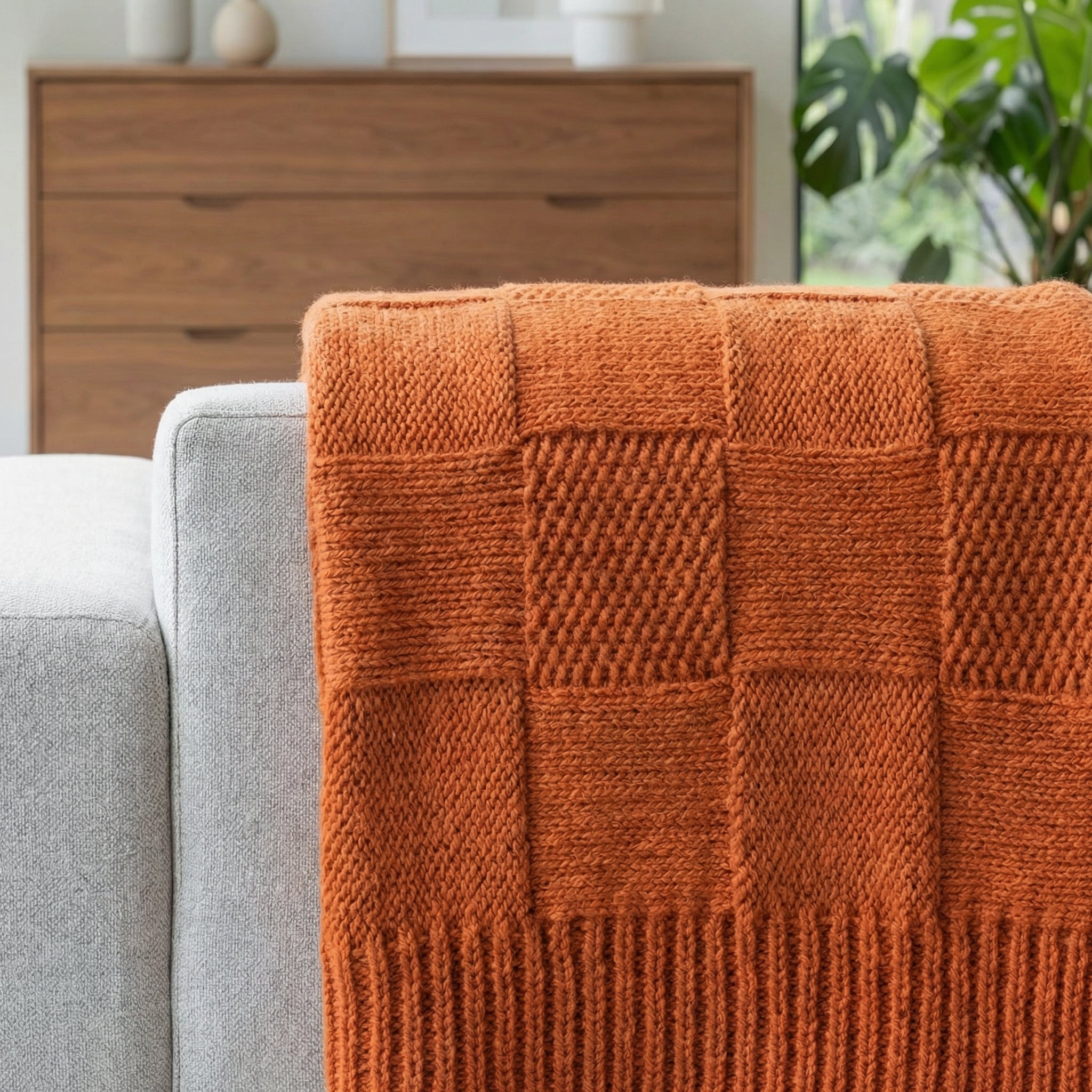 Soft orange knitted cotton blanket with a checkerboard texture draped over a light gray sofa.