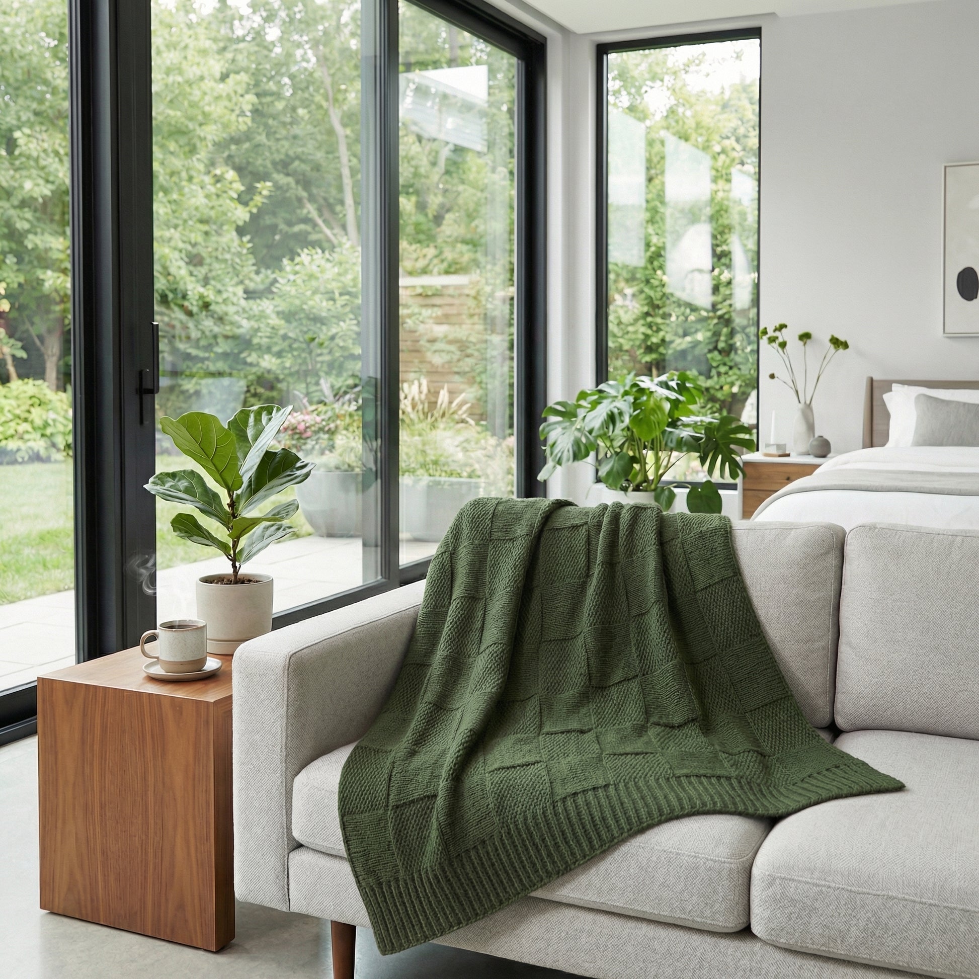 Soft cotton knitted blanket in a rich green, draped over a light gray sofa in a modern room with large windows.