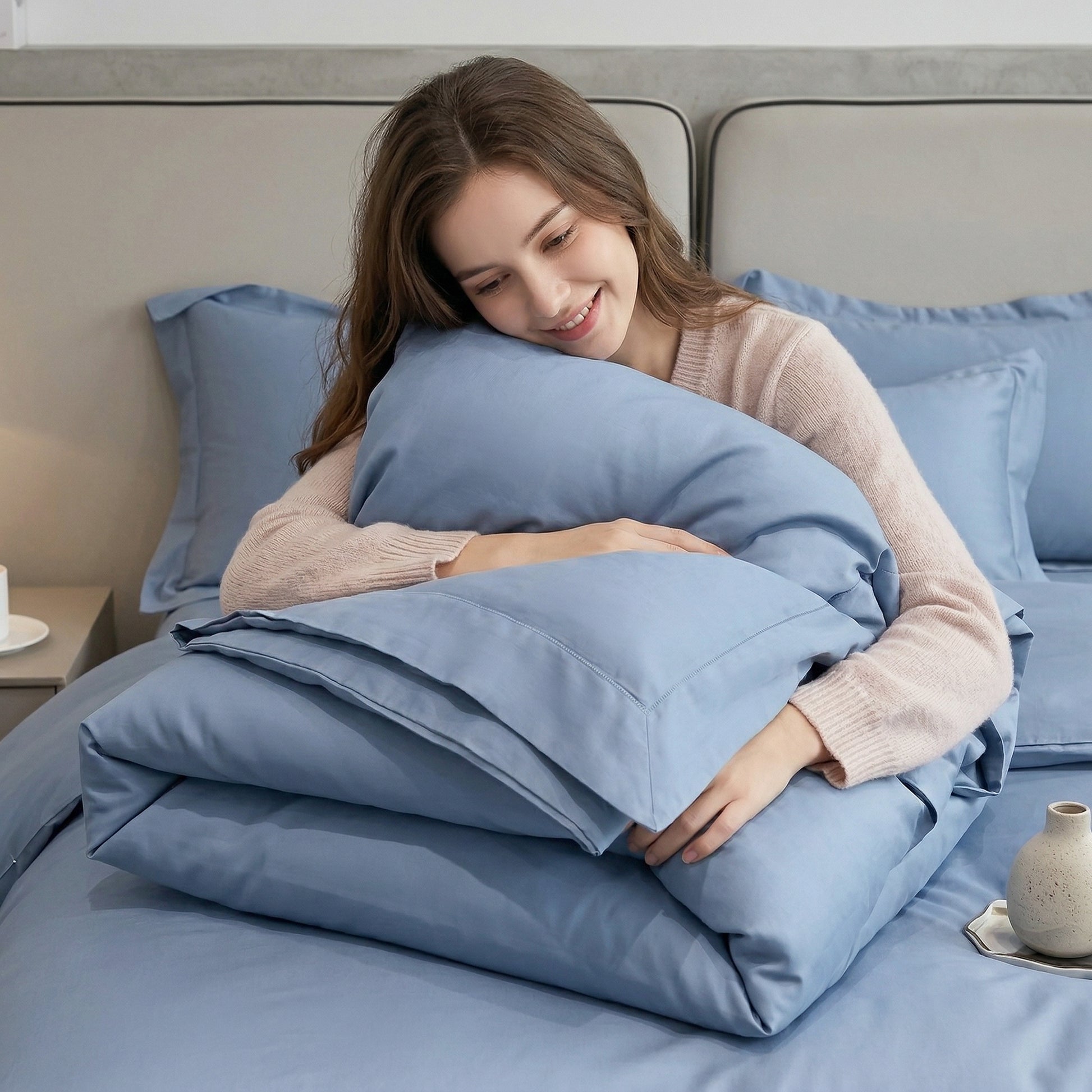 Smiling woman hugging a soft, solid blue cotton duvet cover and pillowcases on a bed.