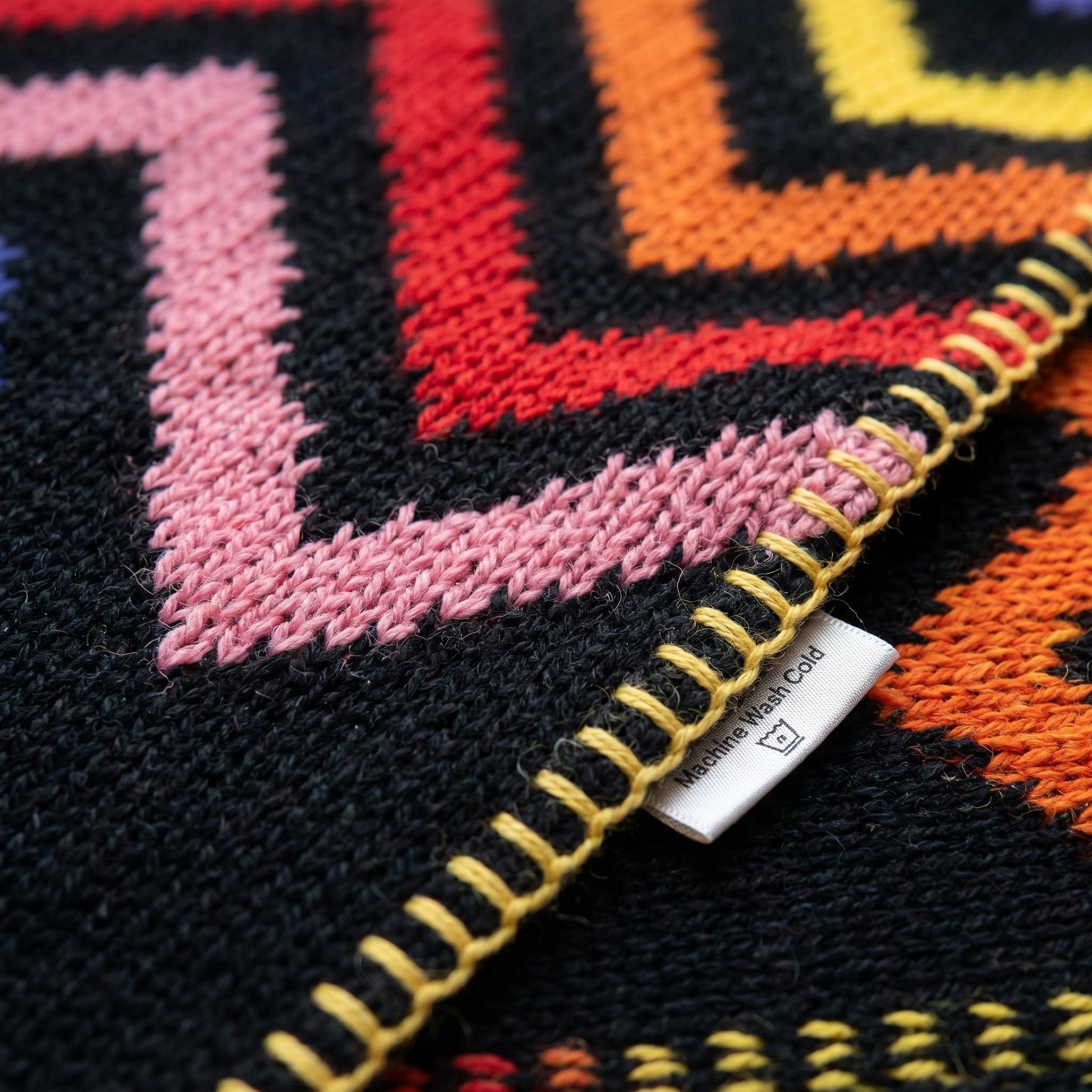Close-up of a Solstice Zig Geometric Throw Blanket with a multicolor zigzag pattern and yellow stitched edge.