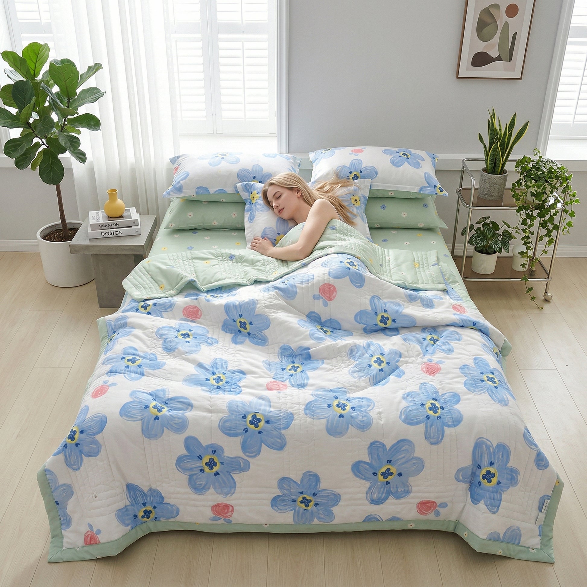 Woman sleeping on a bed with a white quilt featuring large blue floral patterns and light green sheets.