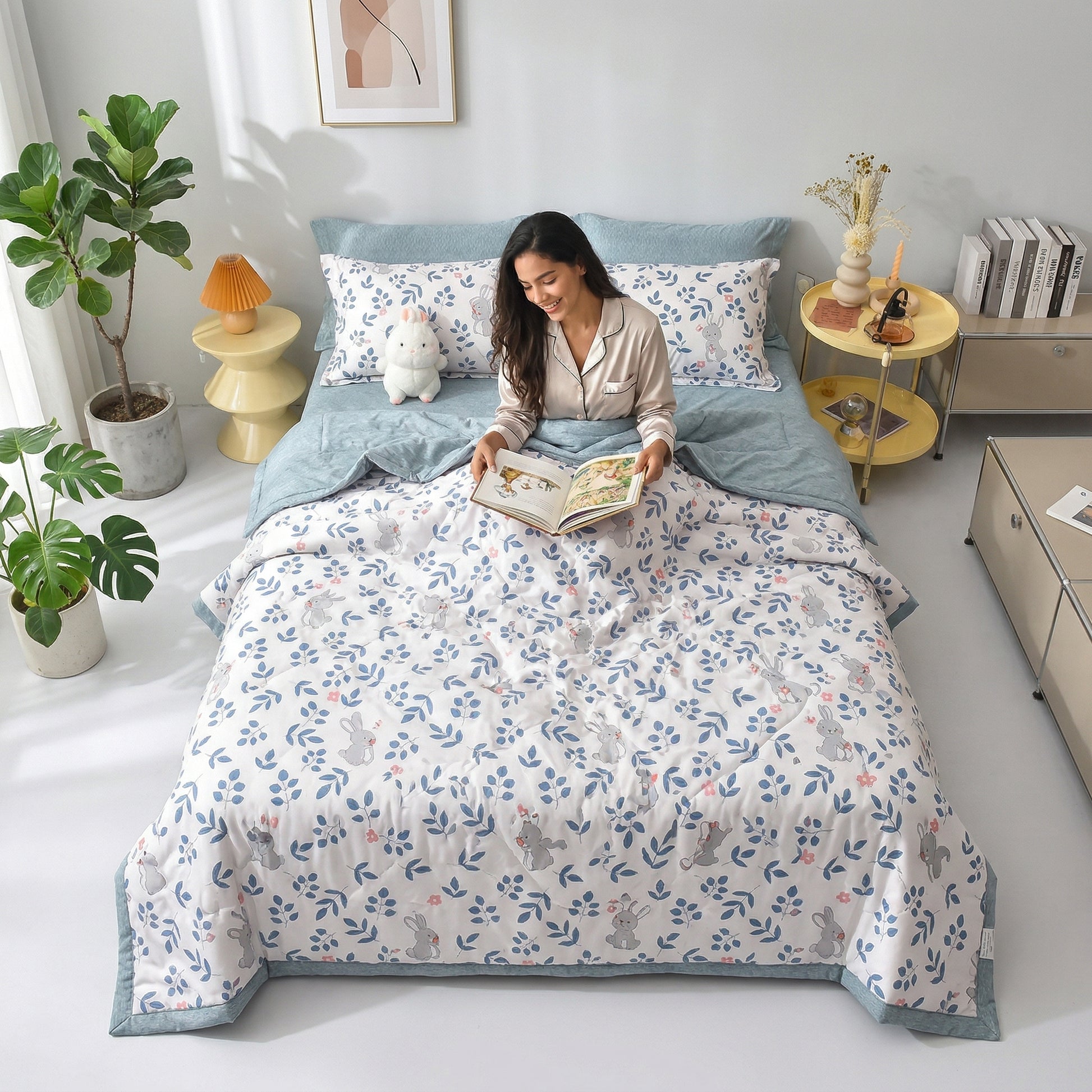 Woman reading in bed with a white and blue Summer Breeze Lightweight Blanket featuring a cute rabbit and leaf pattern.