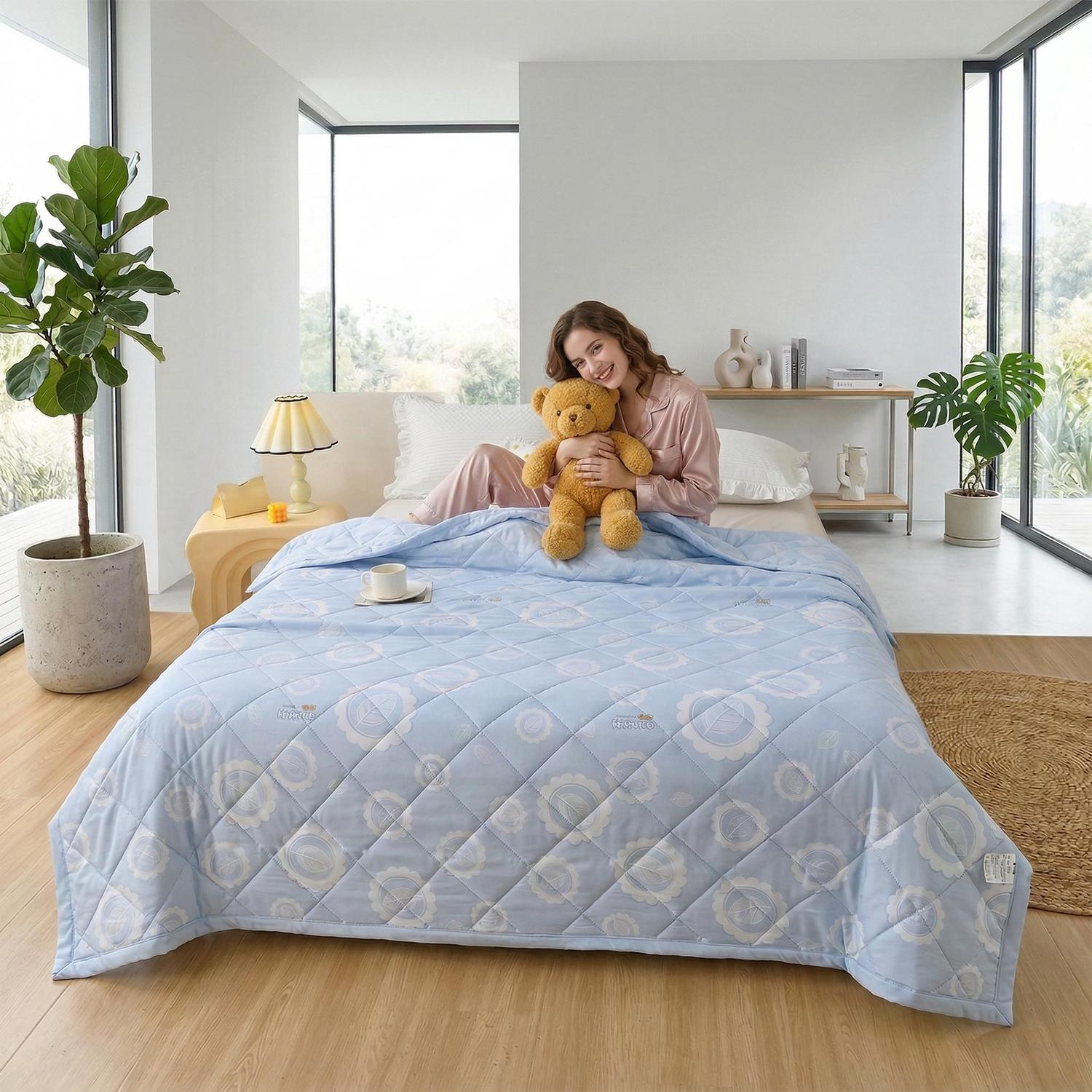 Light blue ultrasonic quilted summer comforter on a bed with a woman holding a teddy bear.