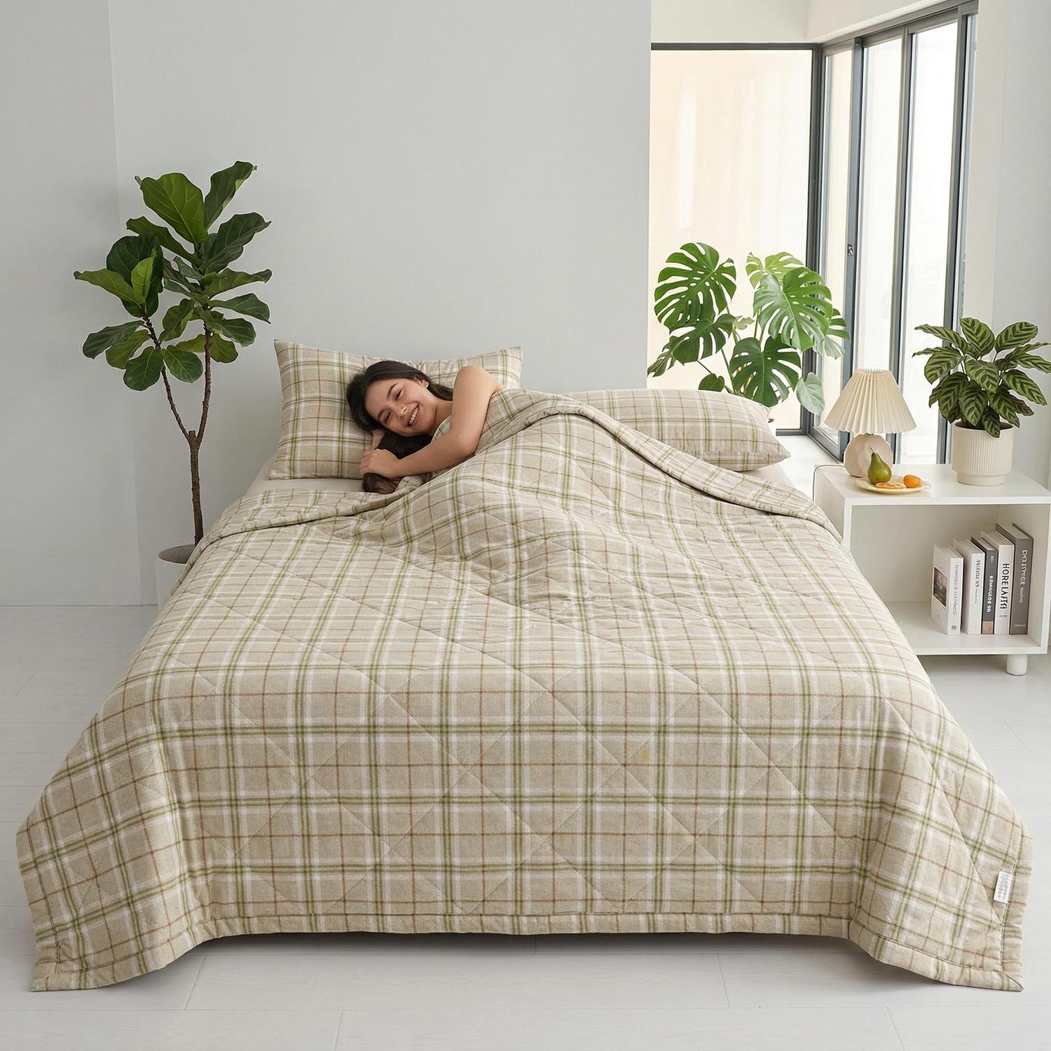 Smiling woman relaxing in a bed with a beige and green plaid ultrasonic quilted summer comforter.