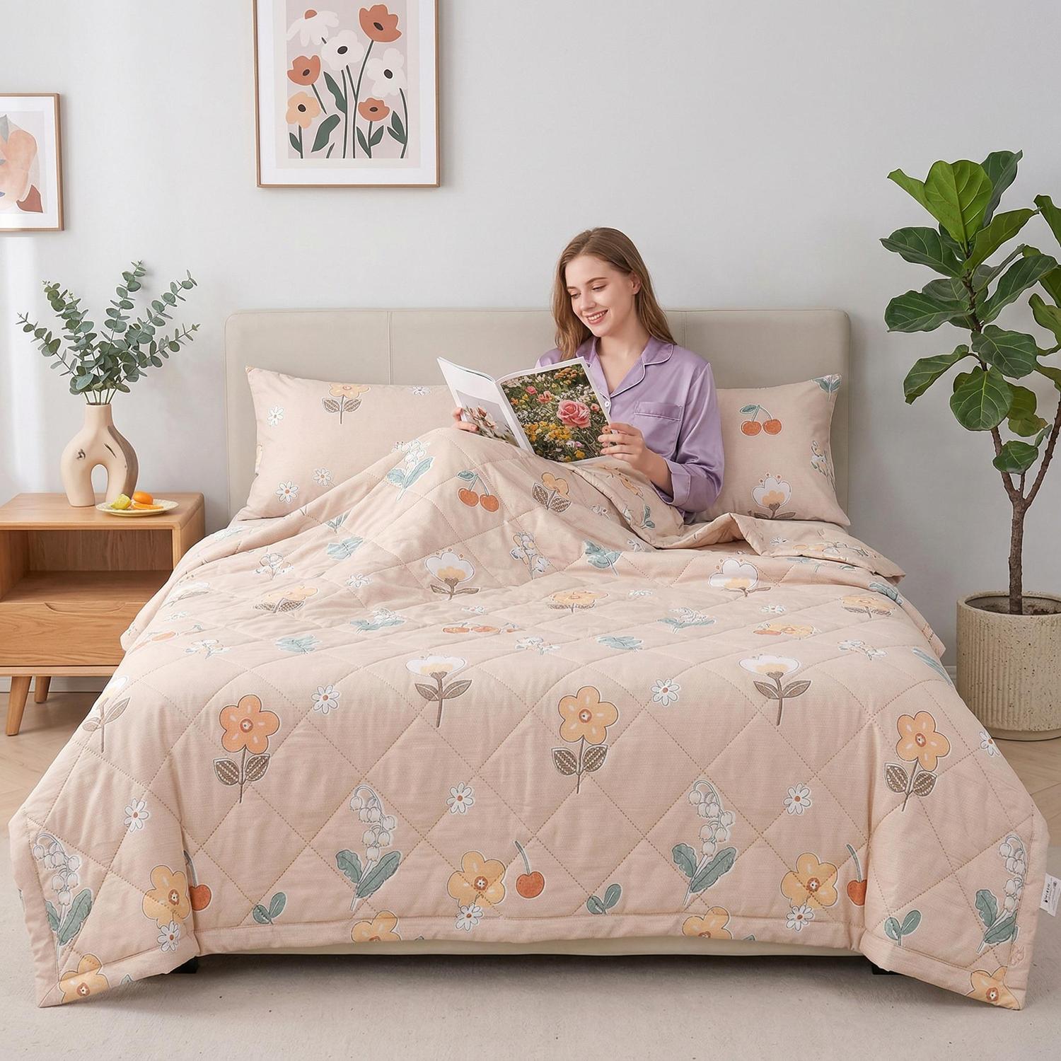 Light pink Summer Comforter with floral and cherry pattern, ultrasonic quilted, on a bed with a woman reading.