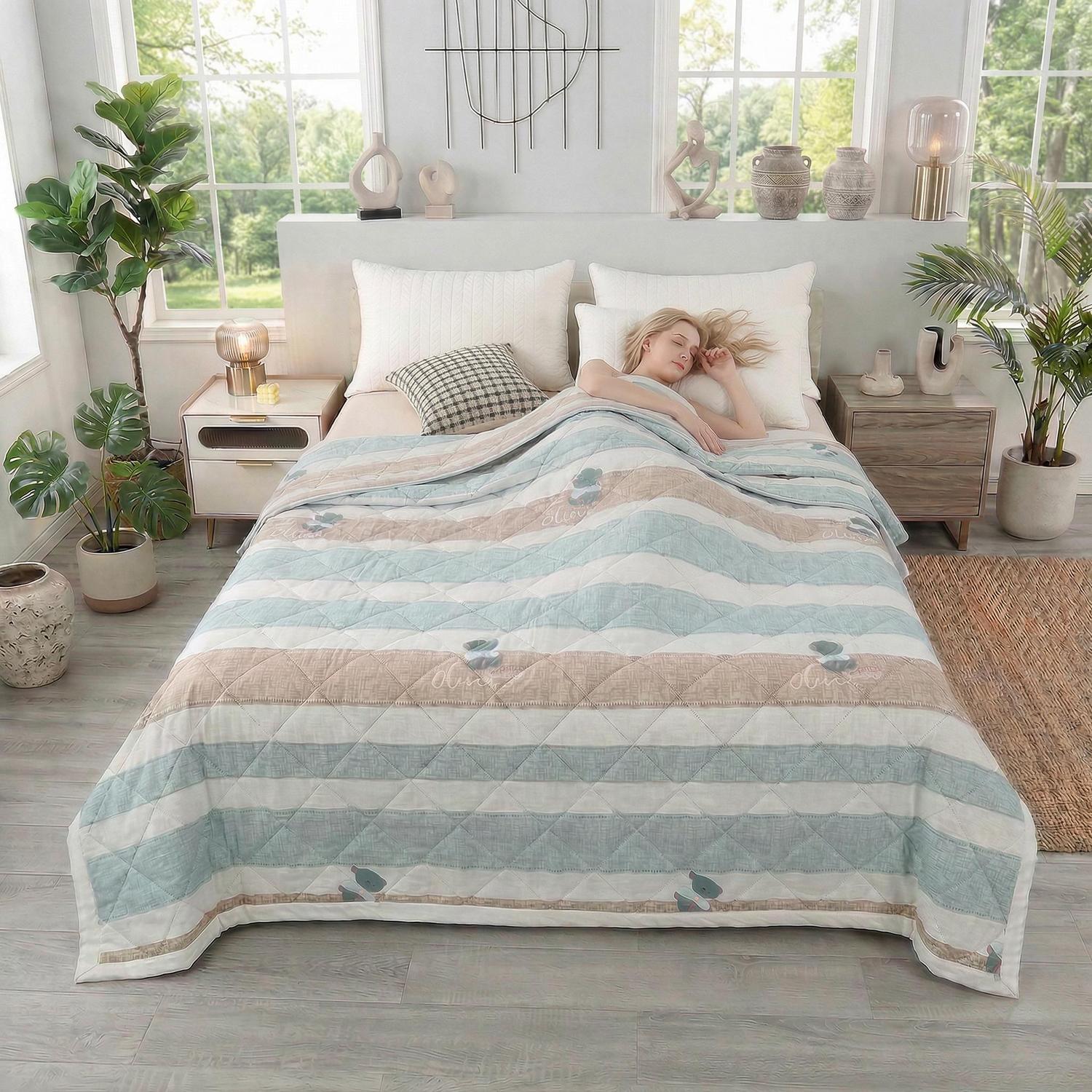 Woman sleeping under a striped blue, beige, and white ultrasonic quilted summer comforter in a bright bedroom.