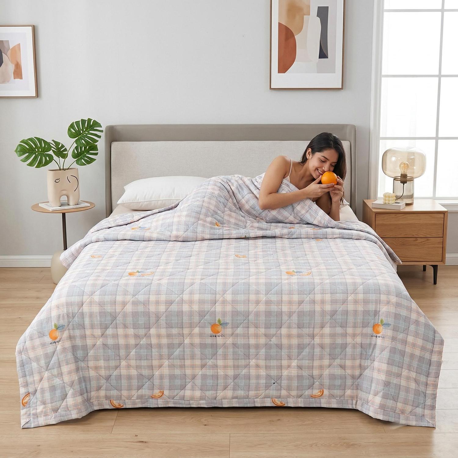 Woman on a bed with a lightweight, plaid ultrasonic quilted comforter featuring orange fruit designs.