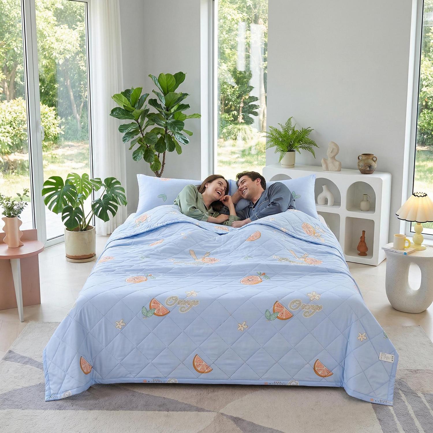 Light blue ultrasonic quilted summer comforter with orange fruit pattern on a bed with a couple.