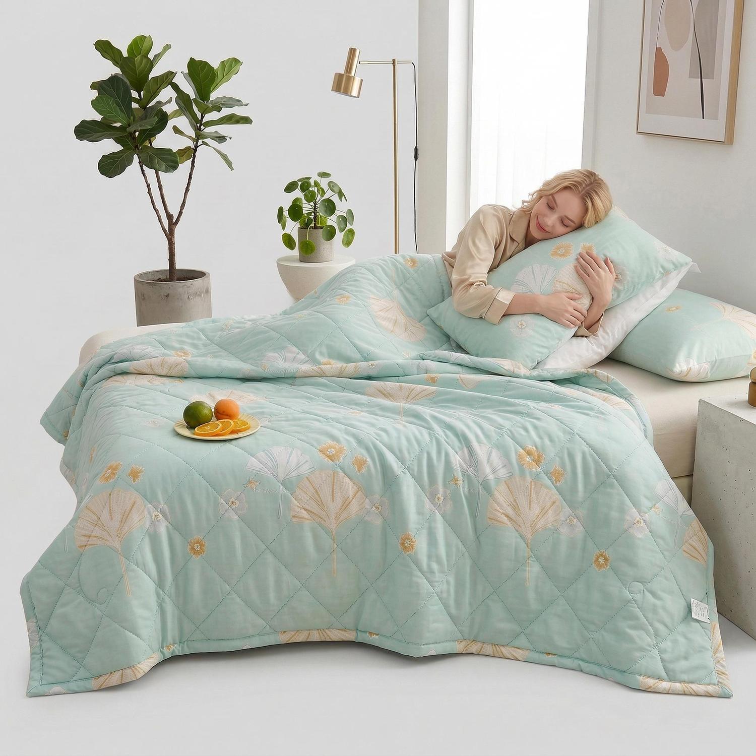 Woman sleeping comfortably under a light blue ultrasonic quilted comforter with a subtle fan and floral pattern.
