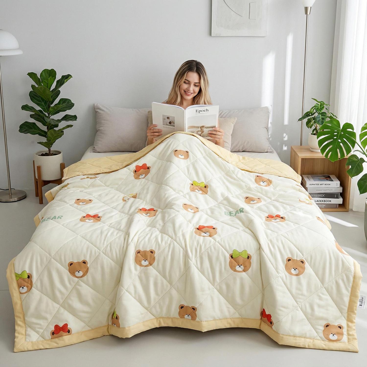 Woman reading in bed under a cream lightweight quilt with colorful bear patterns and a yellow border.