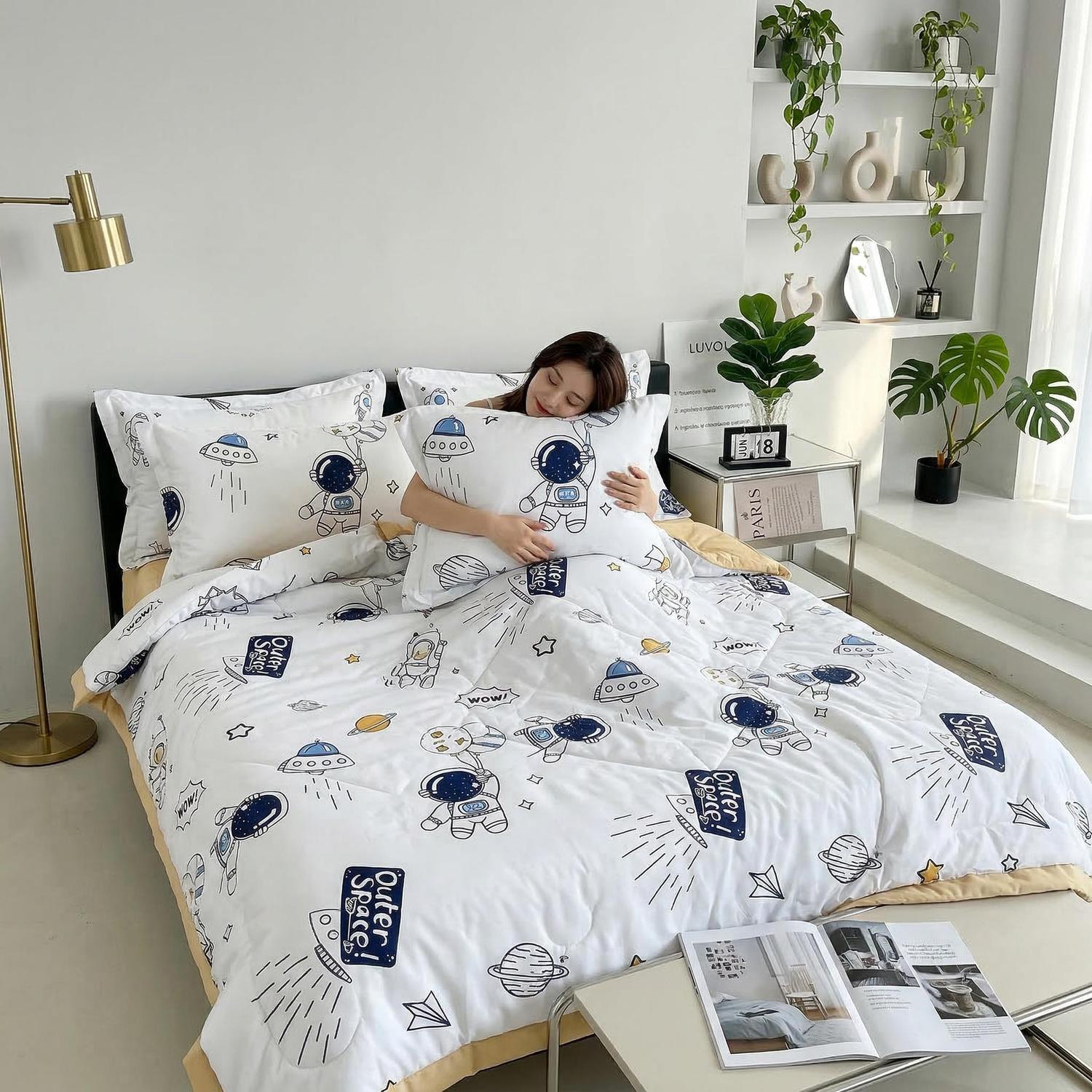 Woman hugging a pillow on a bed with a white ice silk quilt featuring a blue astronaut and spaceship pattern.