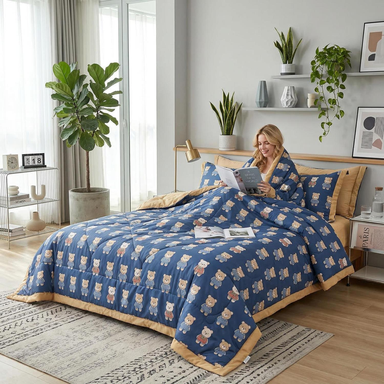 Woman reading in bed with a blue ice silk quilt featuring a cute teddy bear pattern and a tan reverse.