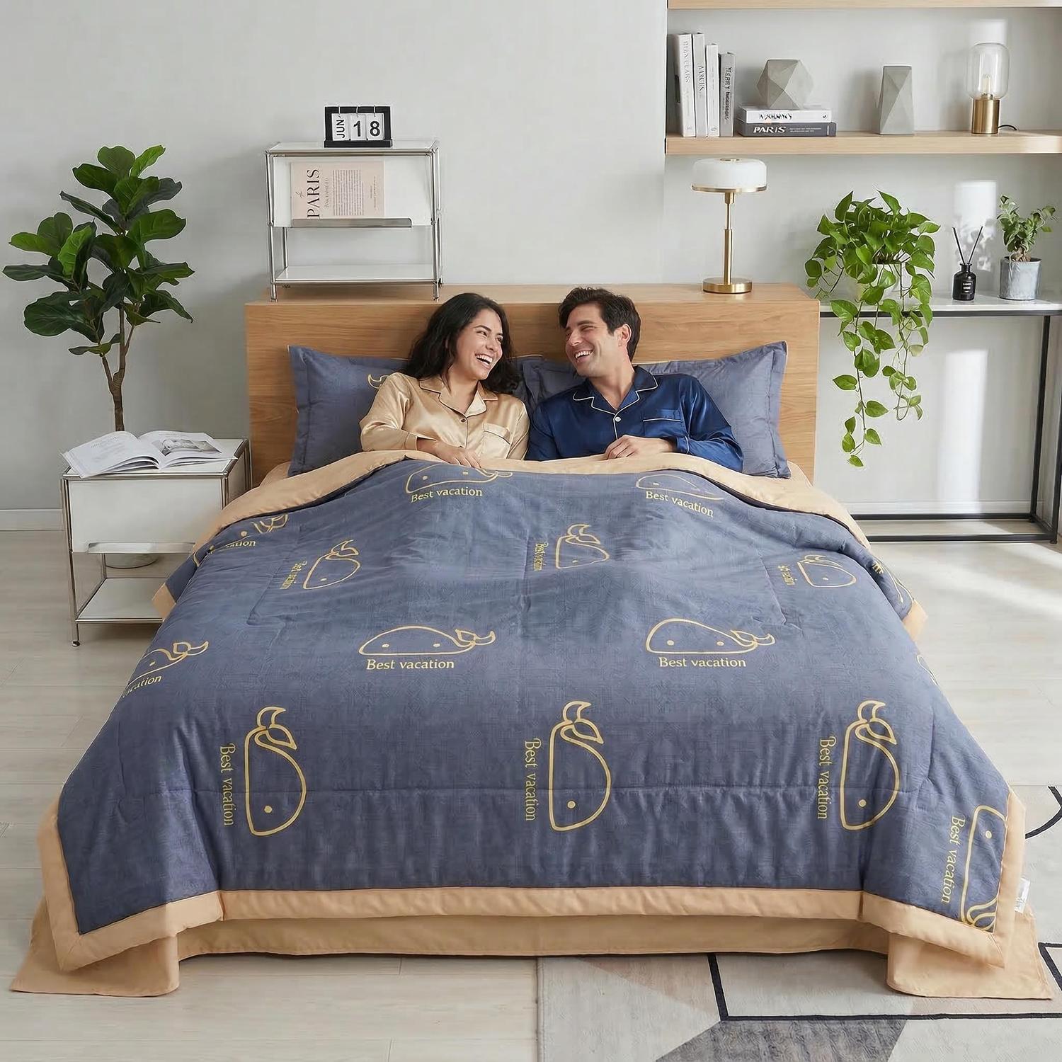 Couple smiling in bed with a blue ice silk quilt featuring yellow whale and "Best vacation" print.