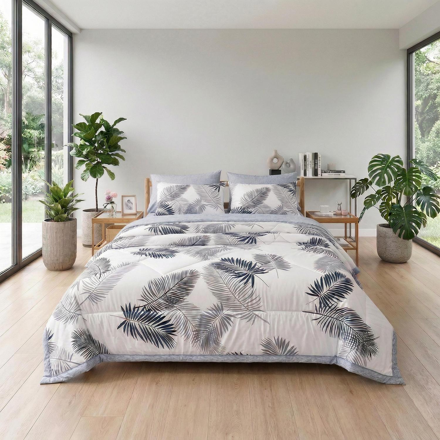 White cooling quilt with blue and gray palm leaf print on a bed in a bright room.