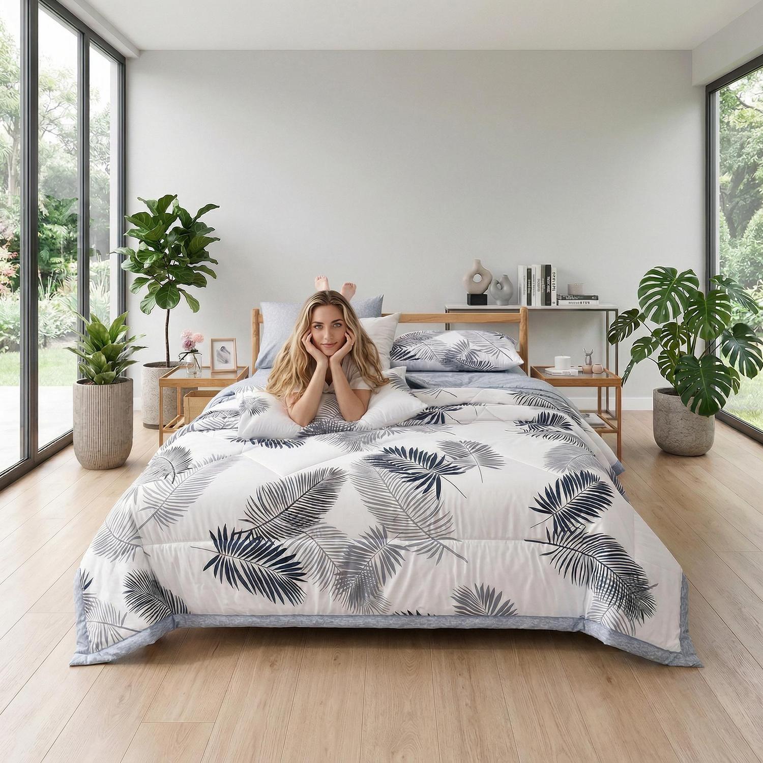 White summer cooling quilt with blue and gray palm leaf print on a bed.