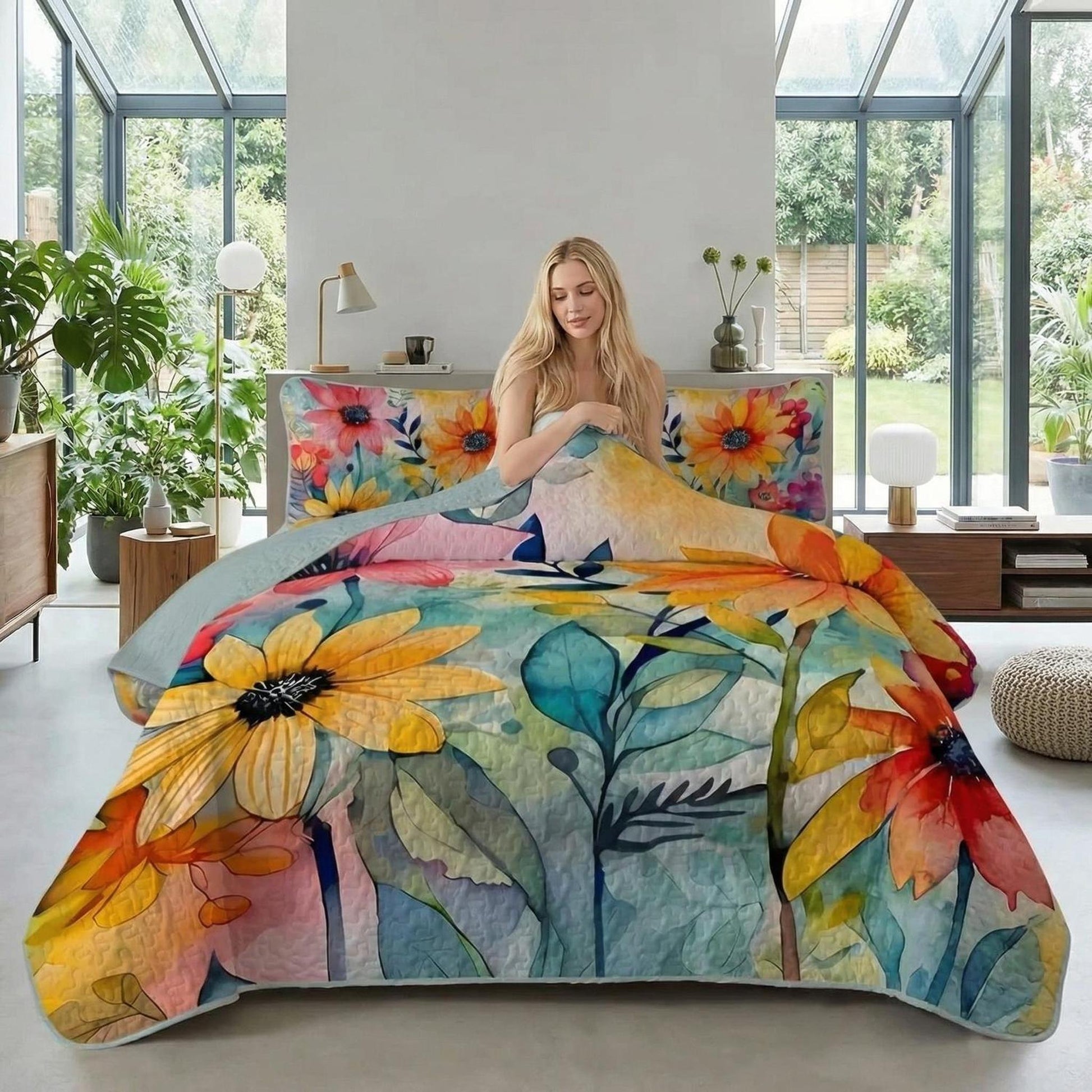 Blonde woman on a bed with a vibrant sunflower printed quilt set, featuring yellow, orange, and blue floral patterns.
