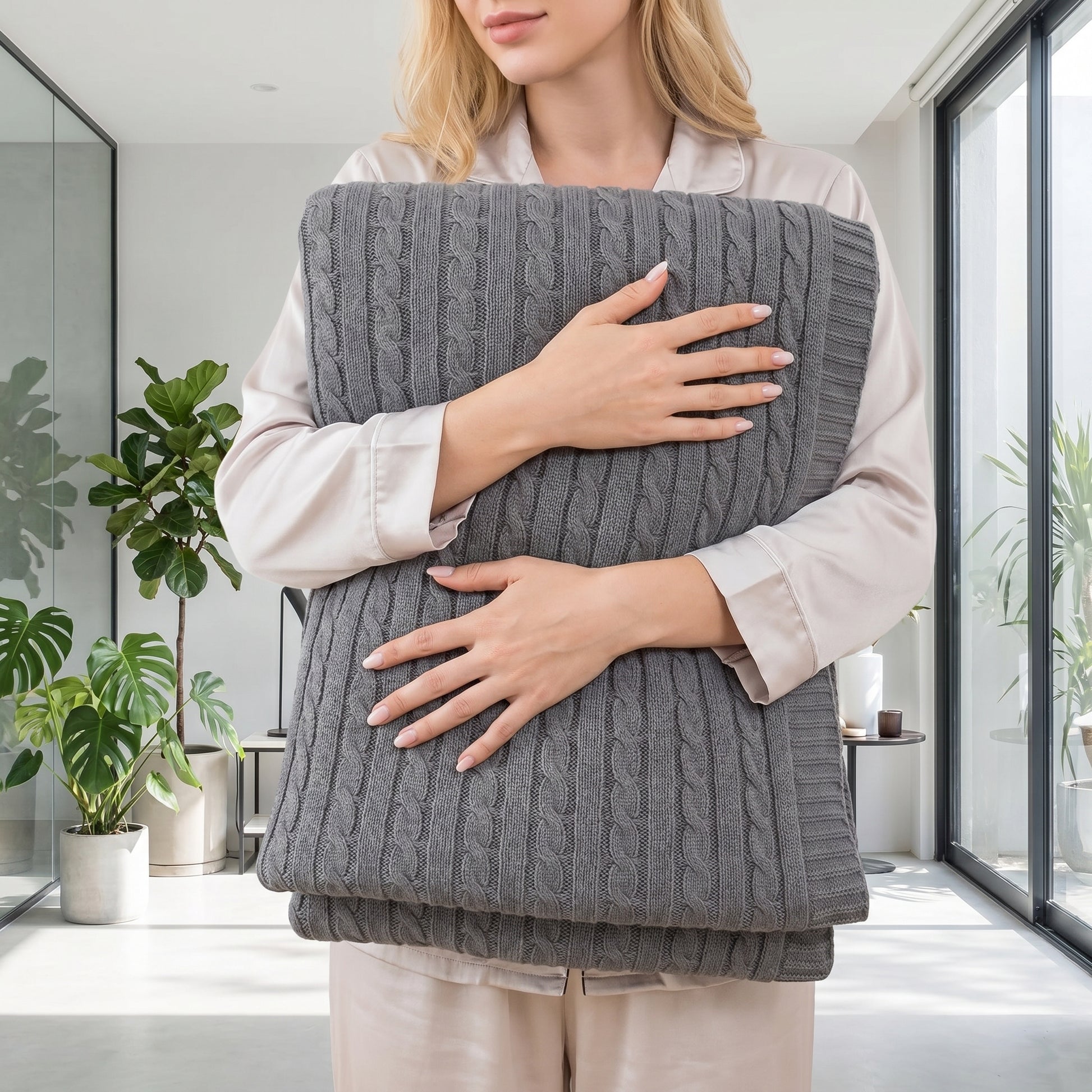 Woman in pajamas holding a folded dark gray textured cable knit cotton throw blanket.