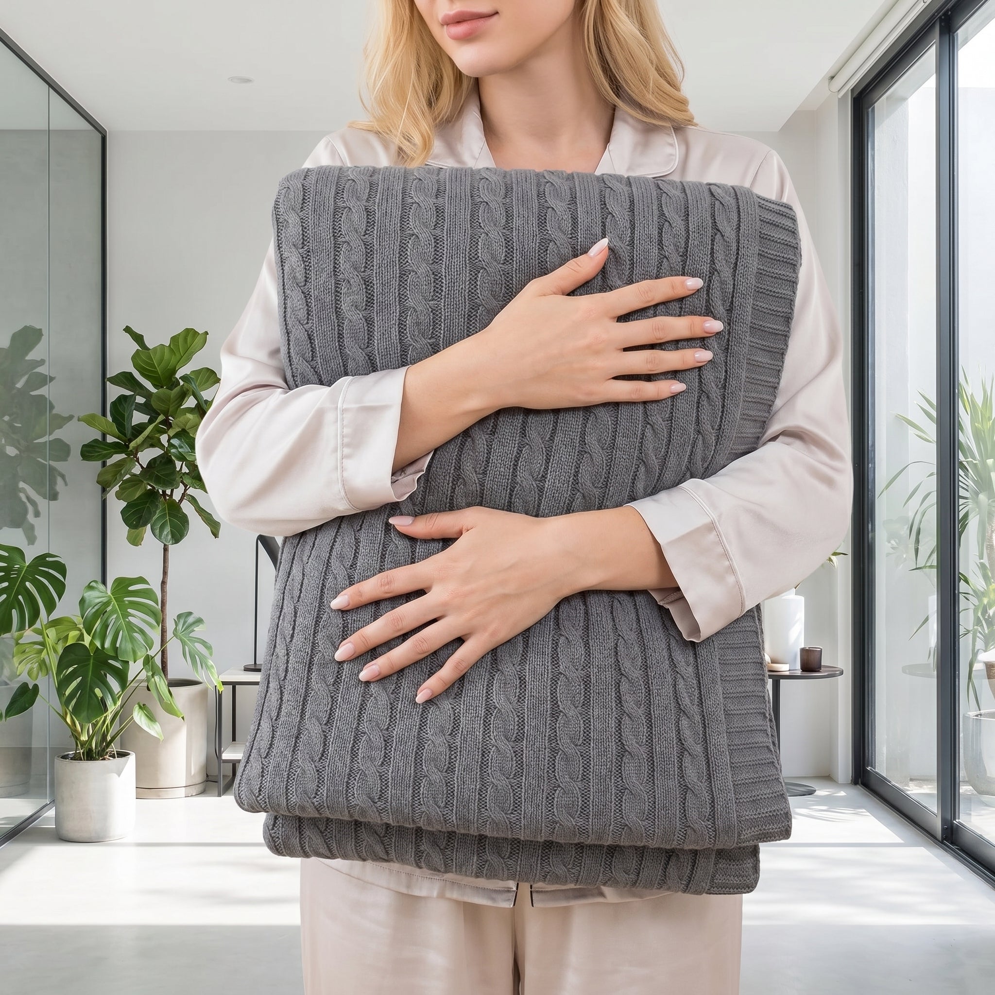 Woman in pajamas holding a folded dark gray textured cable knit cotton throw blanket.