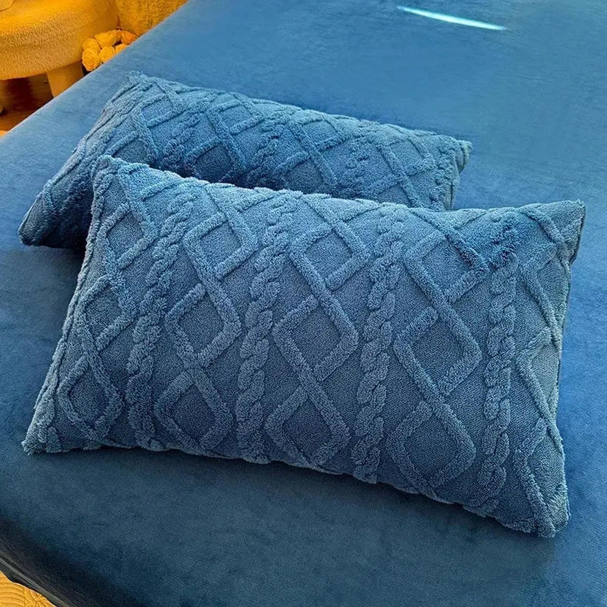 Set of two blue textured velvet pillowcases with a braided diamond pattern on a blue bed.