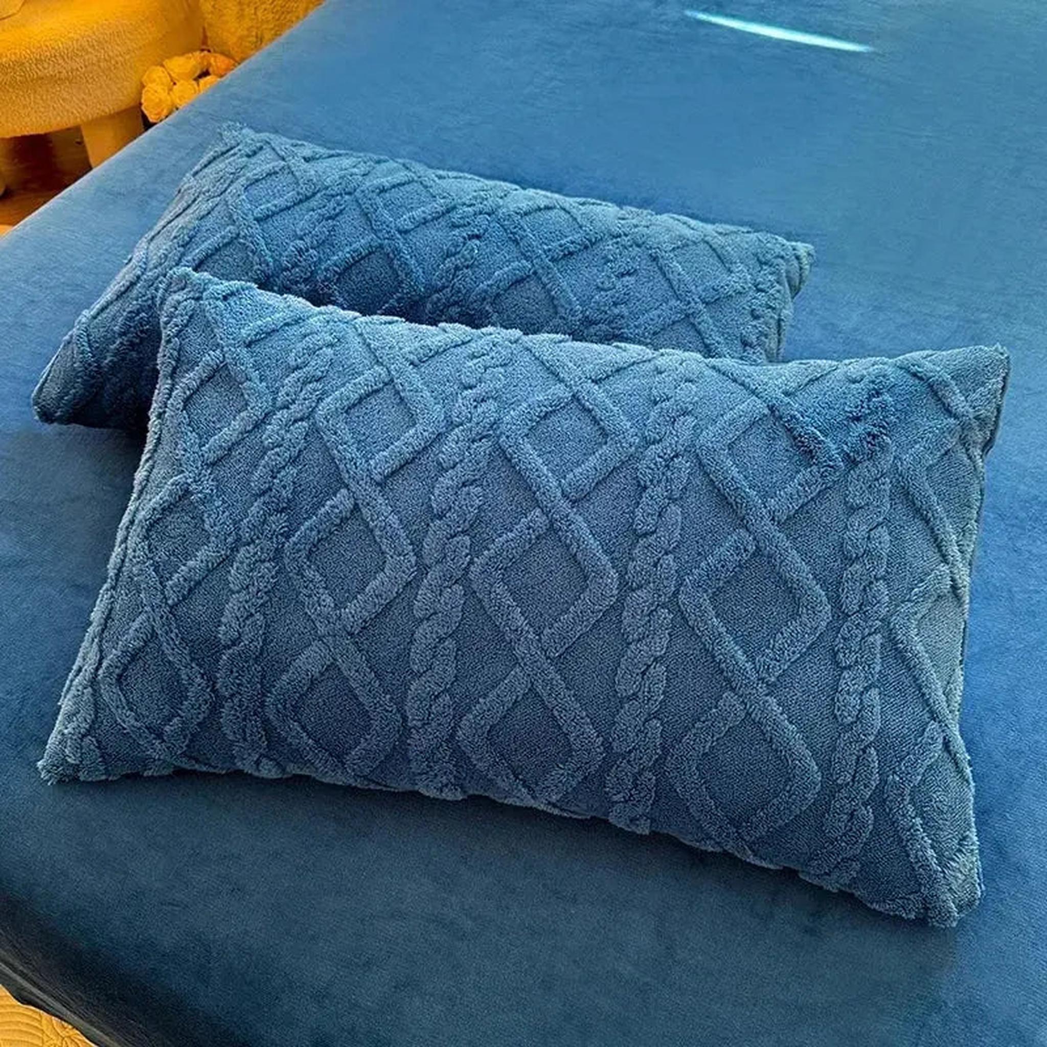 Set of two blue textured velvet pillowcases with a braided diamond pattern on a blue bed.