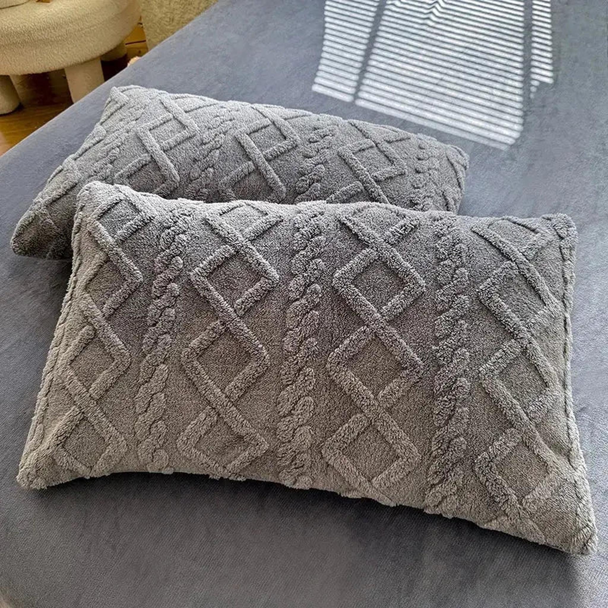 Two gray velvet-like textured pillowcases with a diamond and braid pattern on a bed.