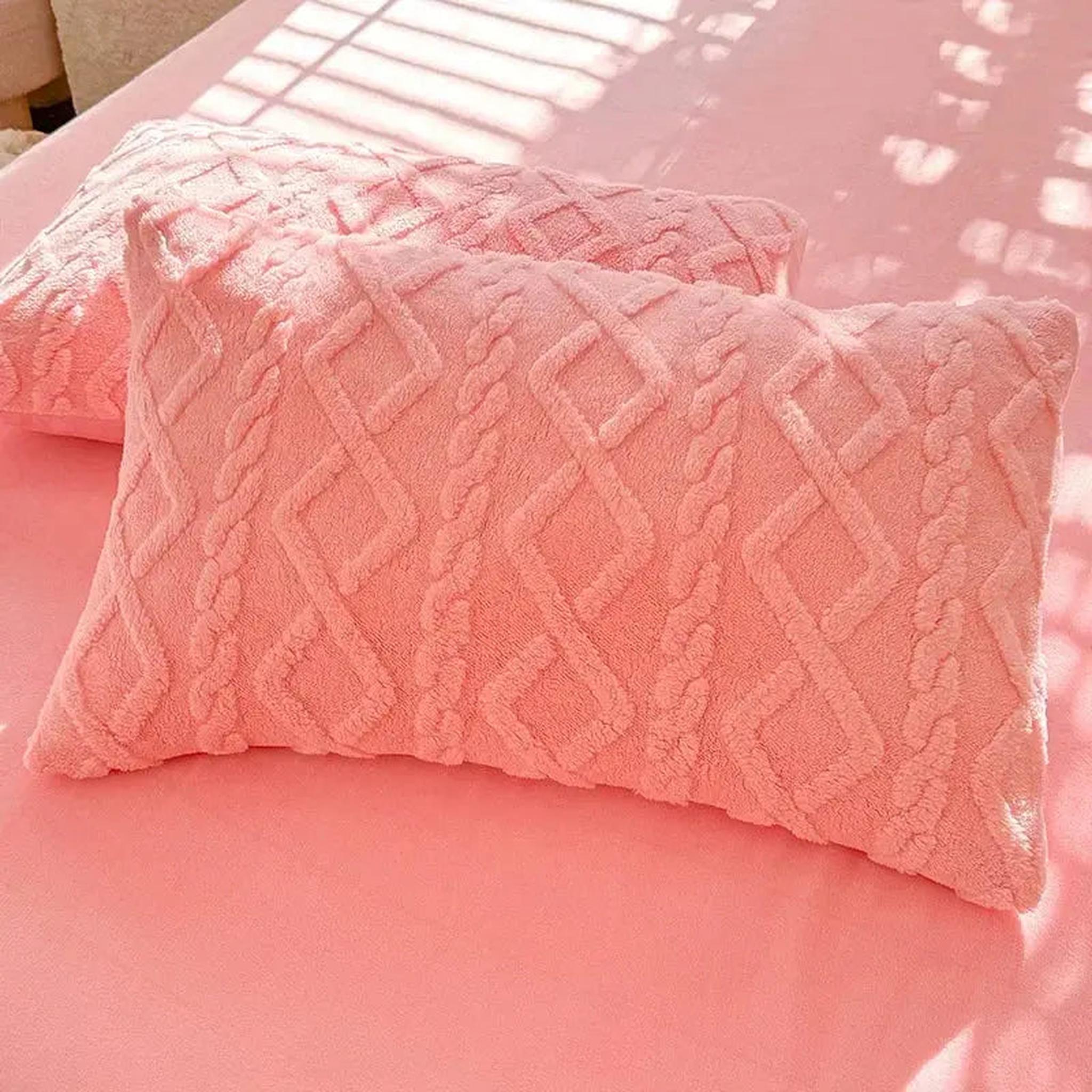 Two soft, plush pink velvet-like pillowcases with a textured cable knit pattern on a pink bed.
